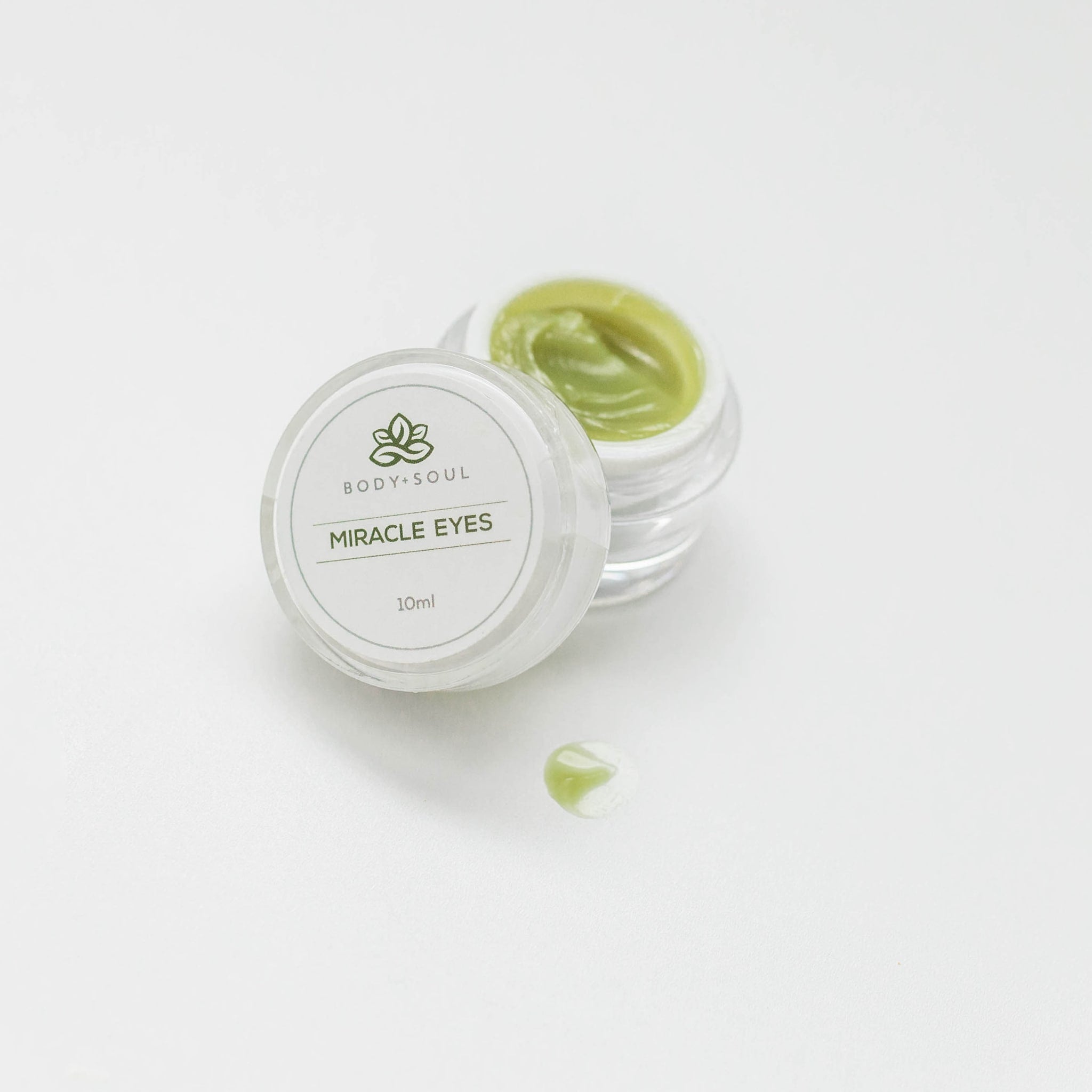 Miracle Eyes cream jar with green cream and Body + Soul label on white surface