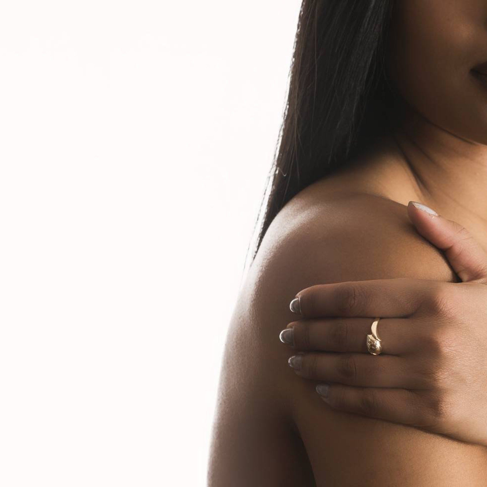 Gold ring, curved design, worn on finger, with woman's arm and shoulder visible