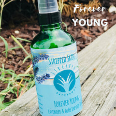 Toner bottle with green glass, blue label, and "Forever Young" text on wooden surface