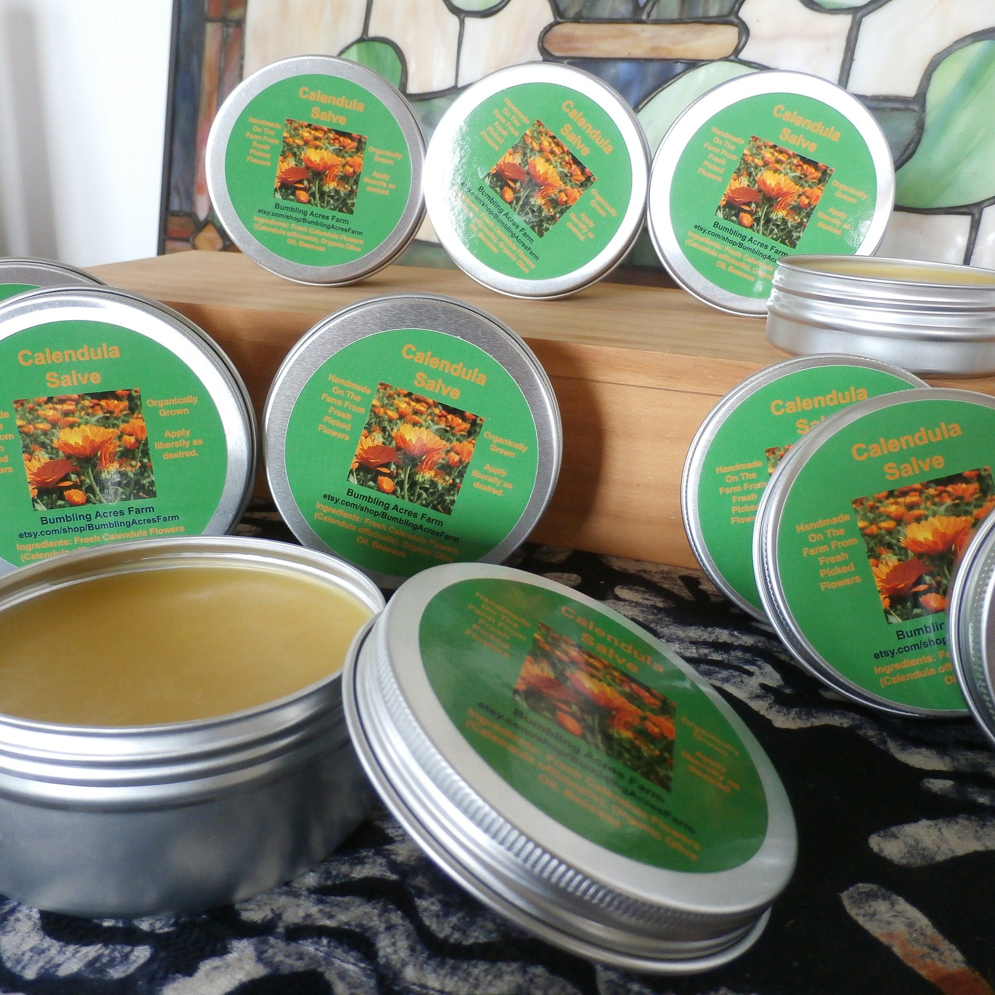 Calendula salve in silver tins with green labels, Bumbling Acres Farm brand visible