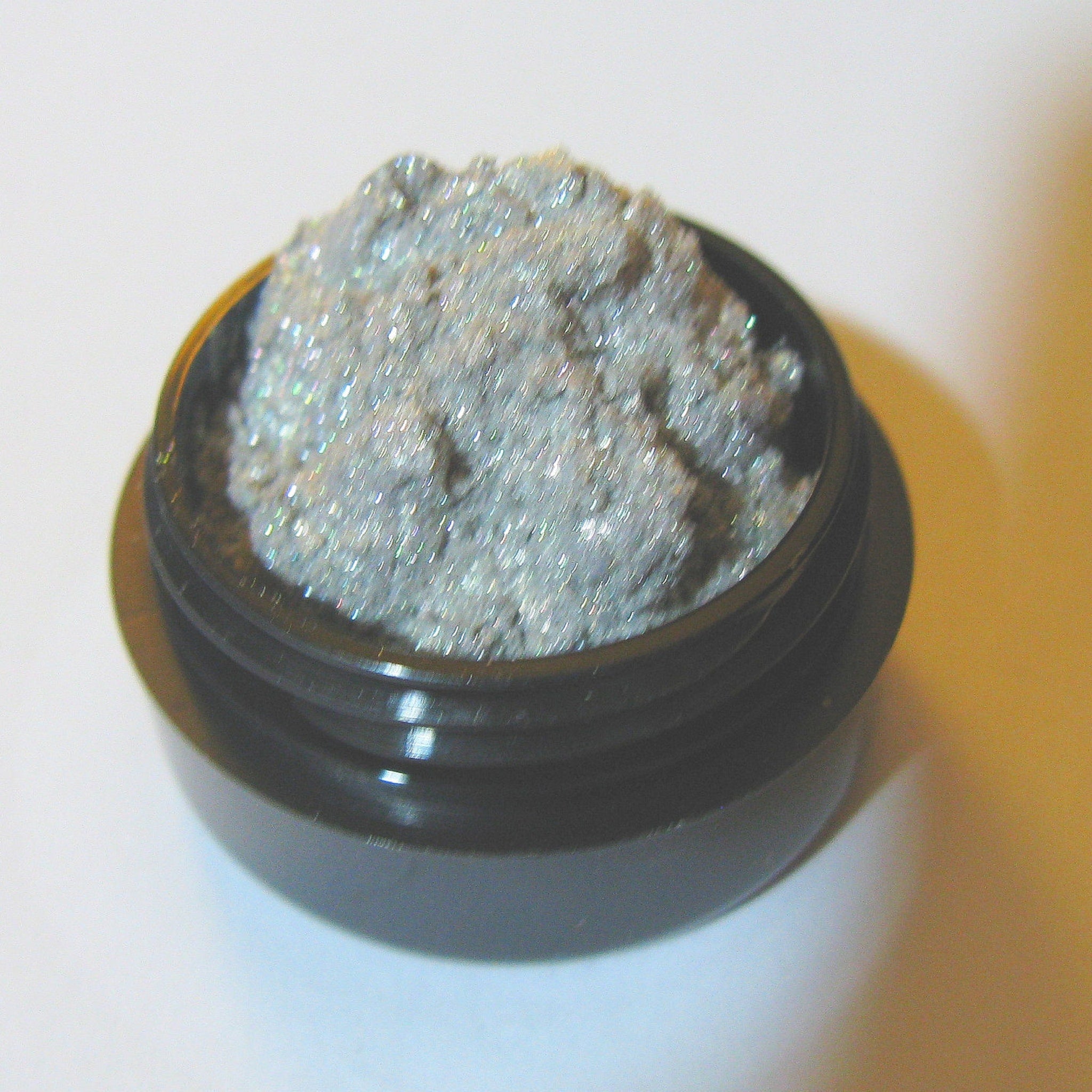 Close-up of platinum silver and gold vegan eyeshadow with intense sparkle in a compact case
