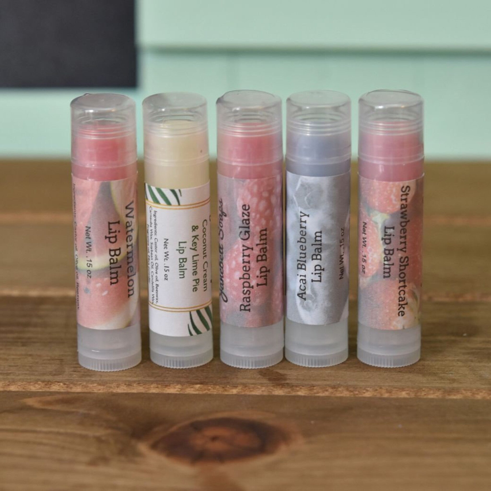 Lip balm tubes with various flavors and labels on wooden surface, JanebellCo branding visible.