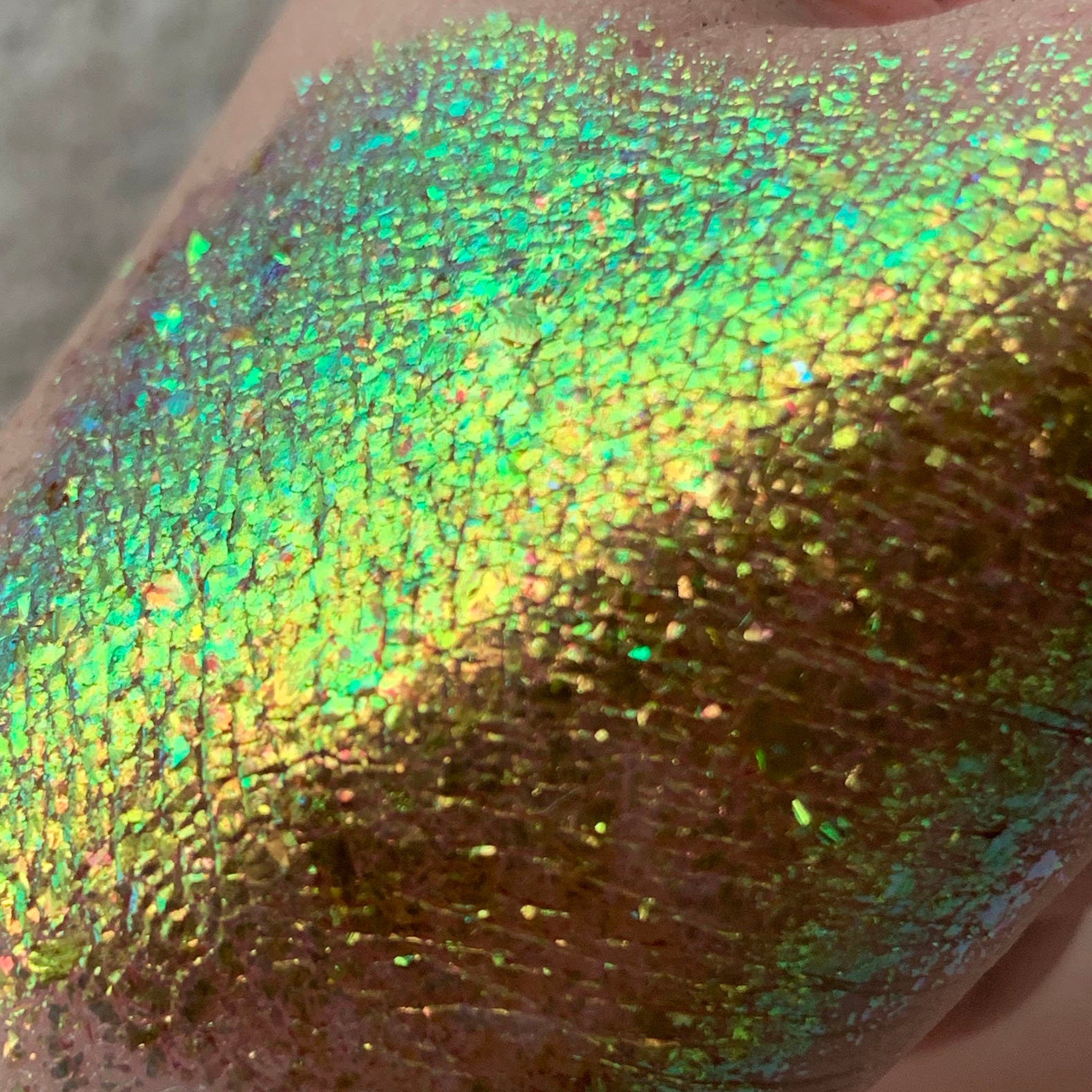 Green and gold iridescent glitter applied to skin, showing texture and color variation.