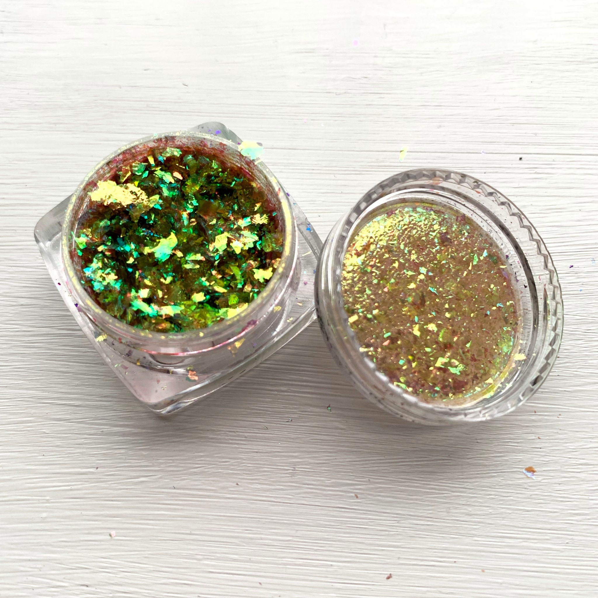 Glitter flakes in green and gold with iridescent shimmer in clear containers on white surface