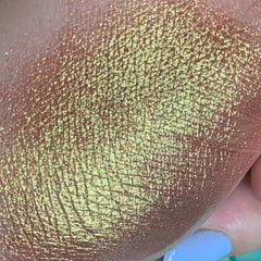 Shimmering eyeshadow swatch, yellow-green iridescent color, textured skin visible, close-up view