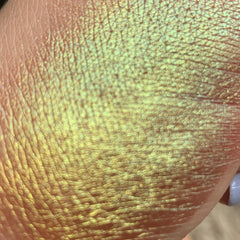 Iridescent shimmer, yellow-green color, textured surface, shown on skin.