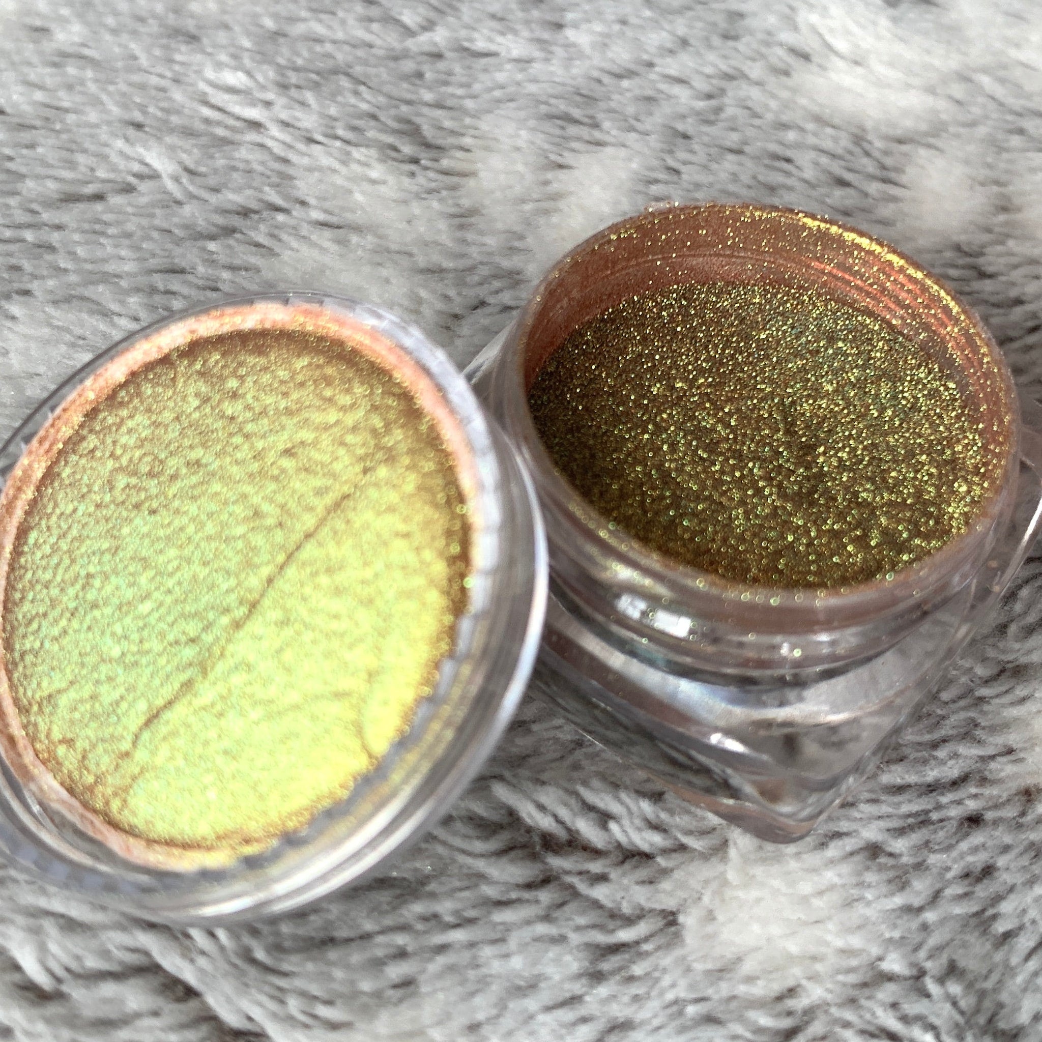 Eyeshadow pots with gold and yellow shimmer, in clear plastic containers on fuzzy surface