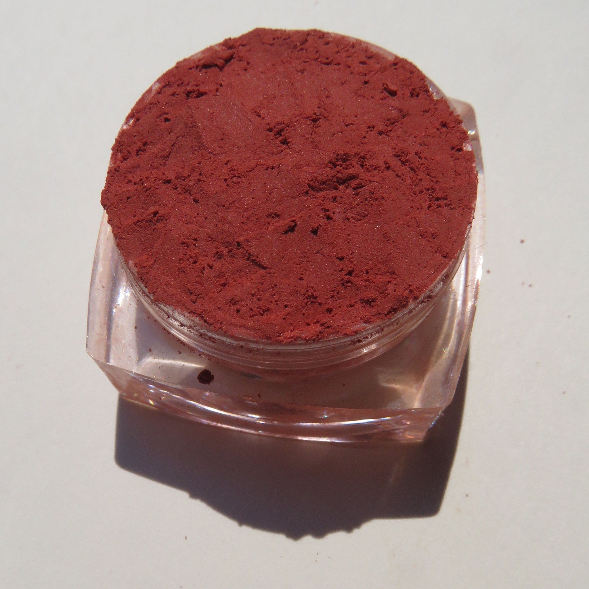 Hand applying vegan matte loose mineral eyeshadow in vibrant orange-red shade KARMA with a fluffy brush