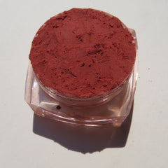 Hand applying vegan matte loose mineral eyeshadow in vibrant orange-red shade KARMA with a fluffy brush