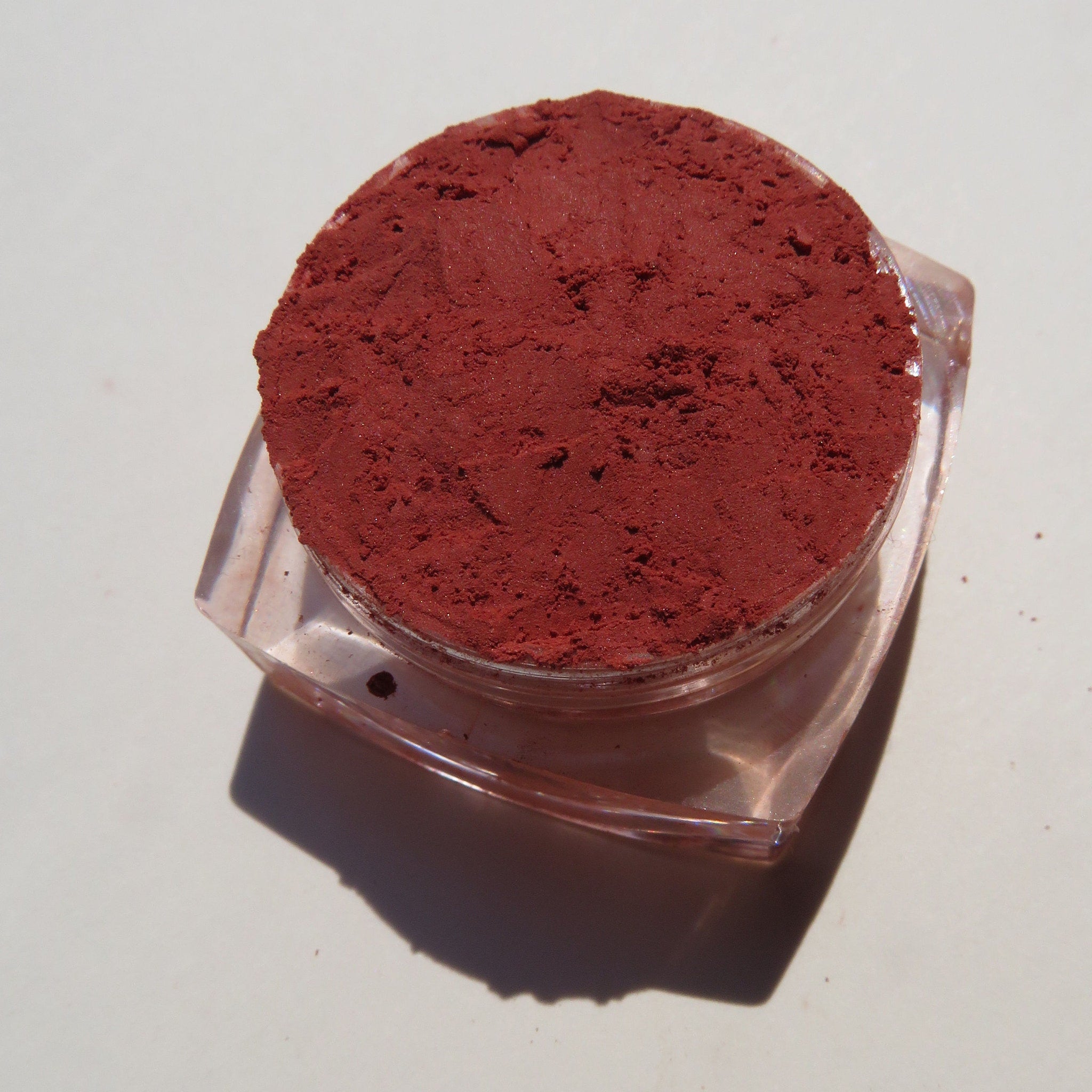 Close-up of vibrant orange-red loose mineral eyeshadow with matte finish, showcasing fine powder texture in a small jar.