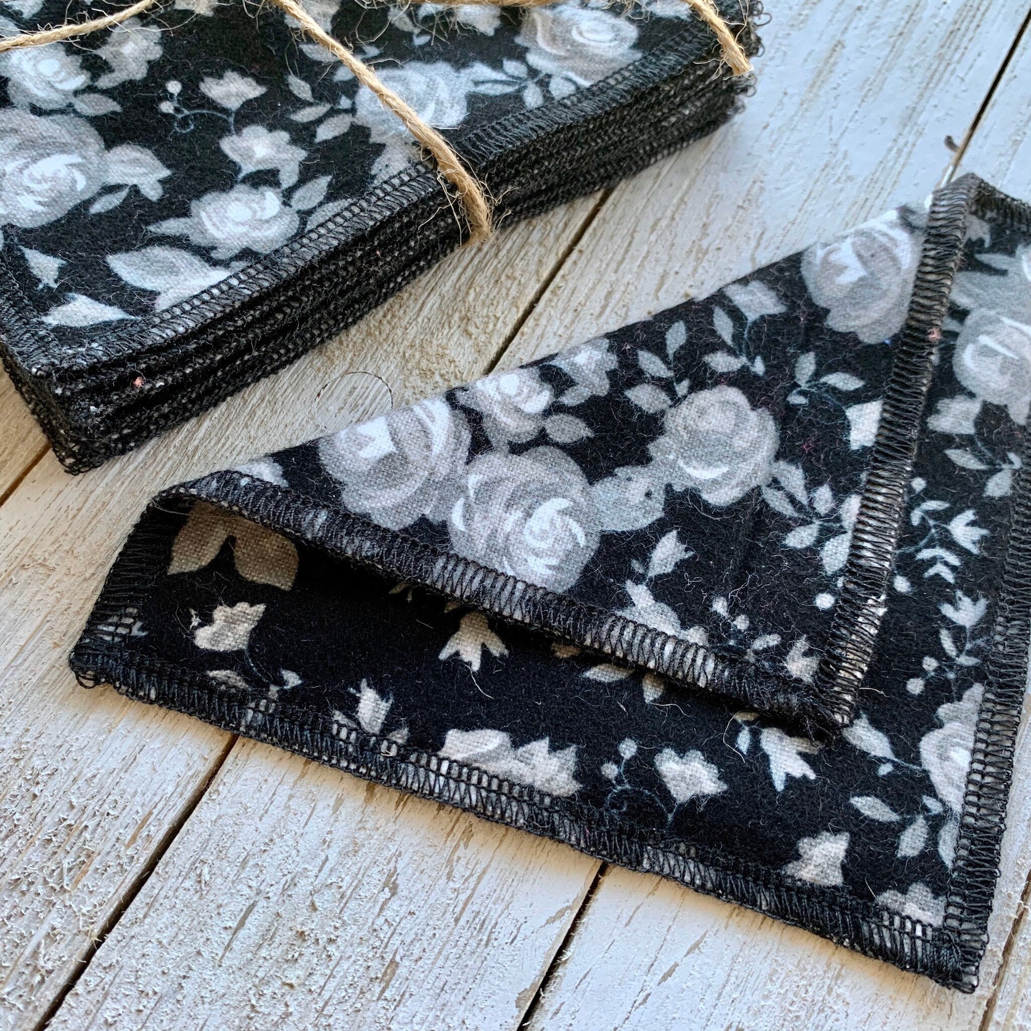 Reusable cloth pads, black floral pattern with gray roses, stacked on wood surface