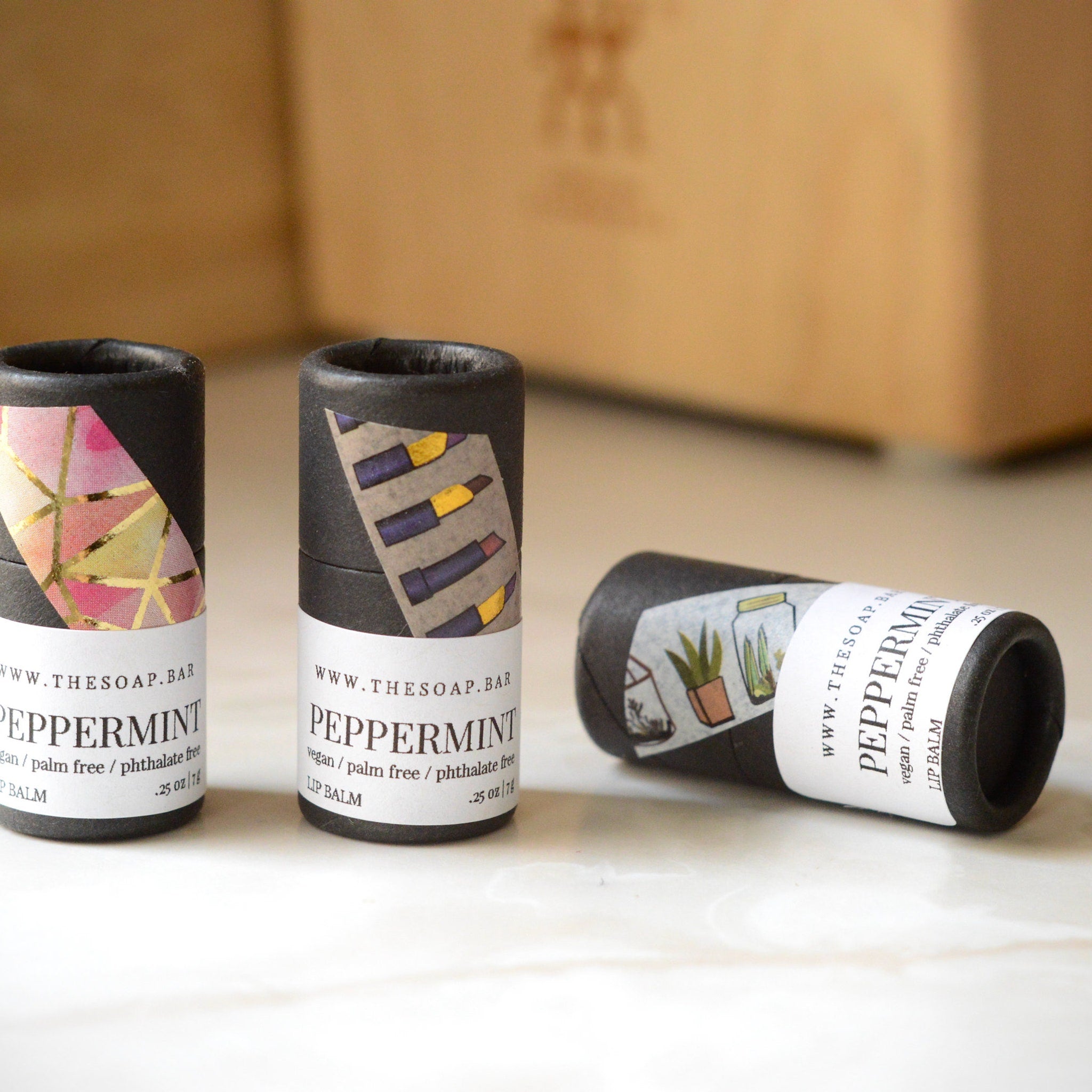 Lip balm tubes with black paper, patterned labels, and white text from The Soap Bar brand