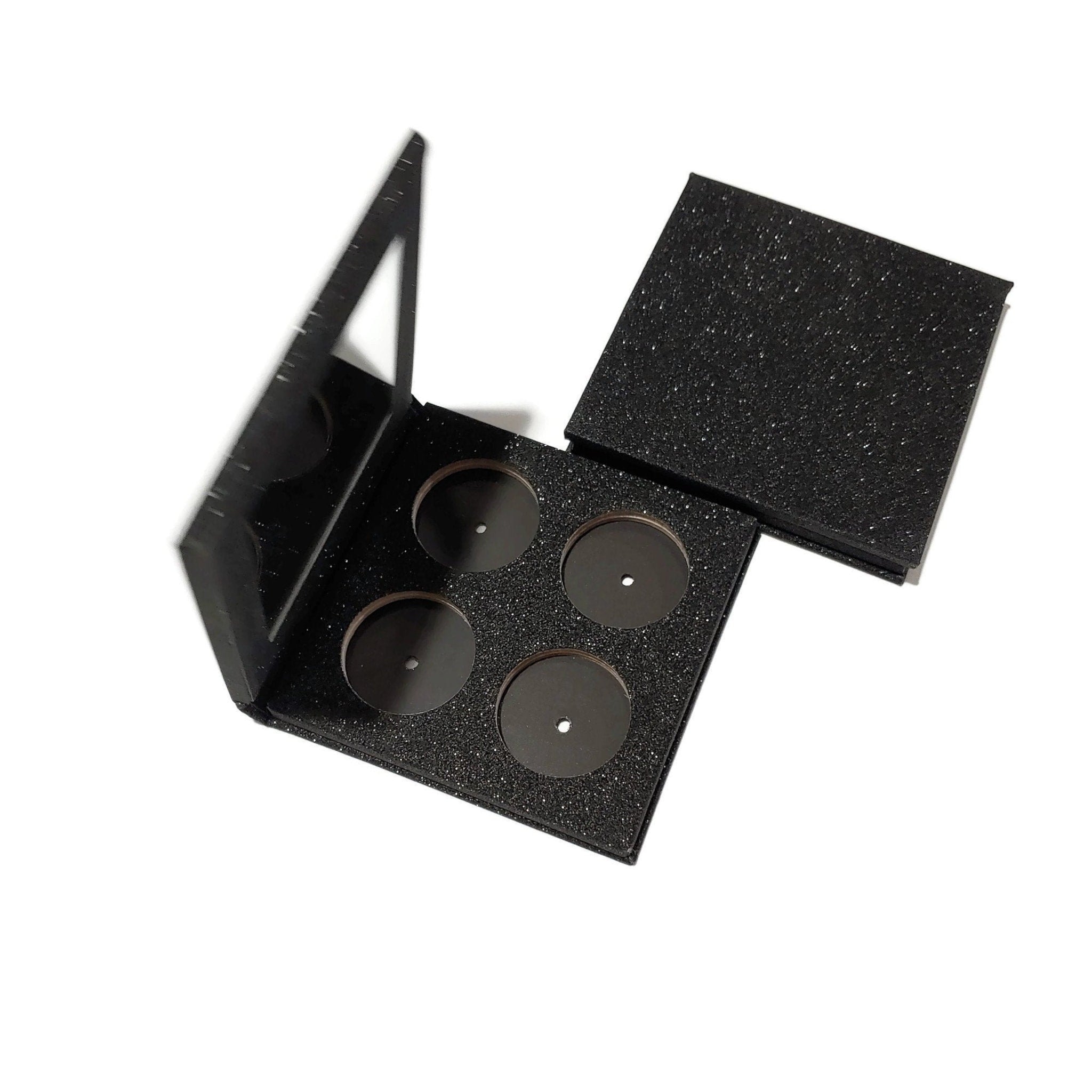 Empty makeup palette with black glitter material and mirror lid open, showing four empty pans