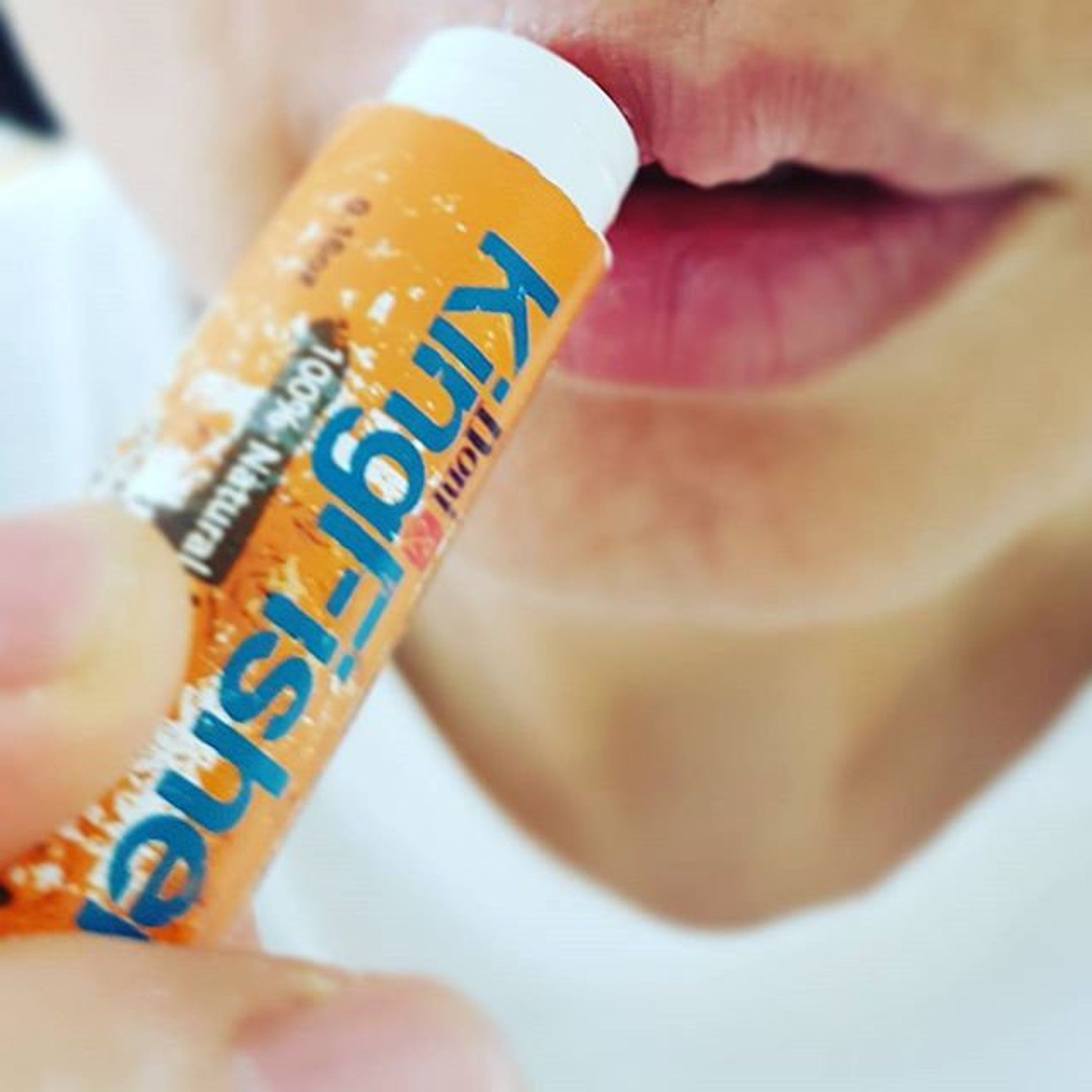 Lip balm tube with orange, blue, and white colors, held near lips, Kingfisher brand visible
