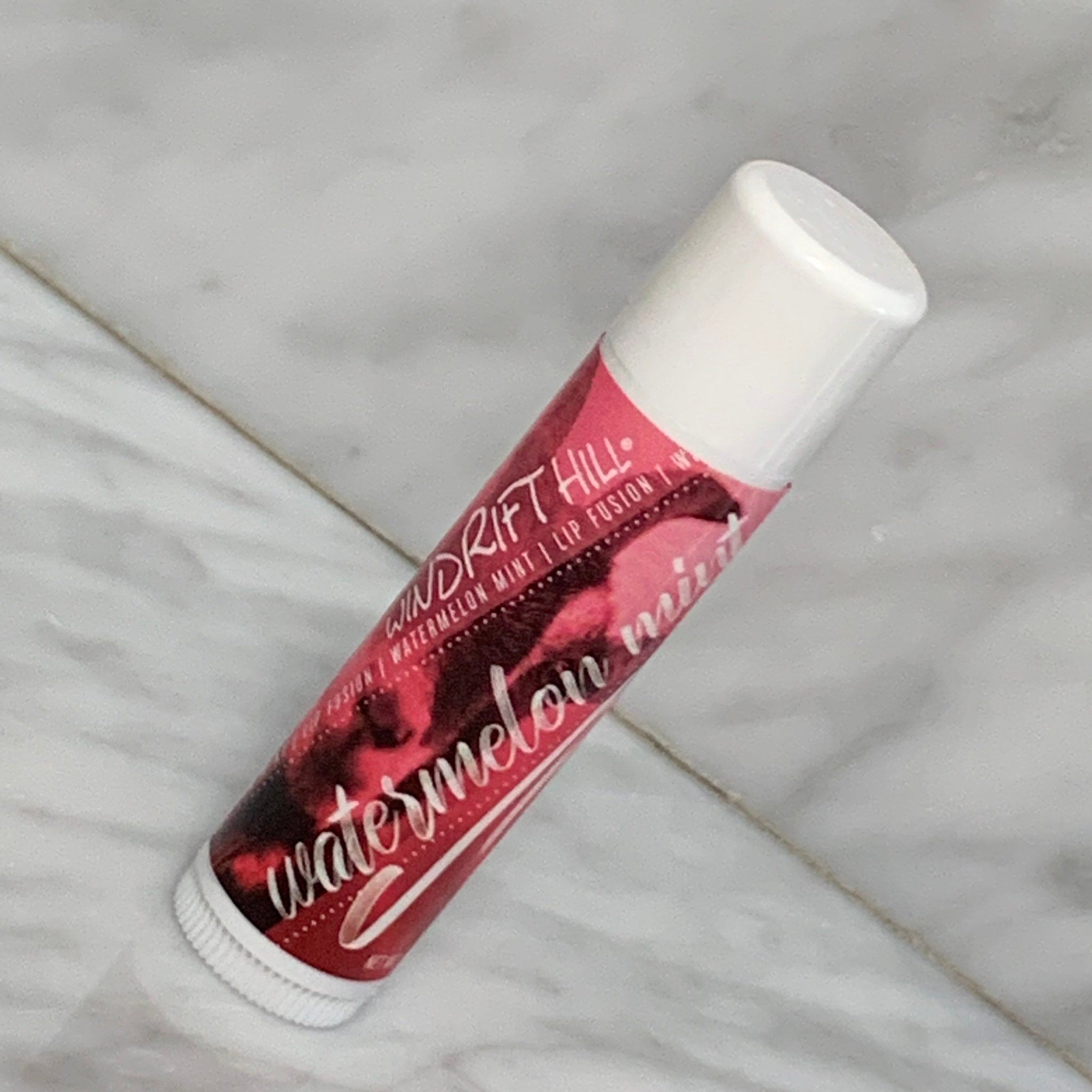 Lip balm tube with white cap, red and black patterned label, "Watermelon Mint" text