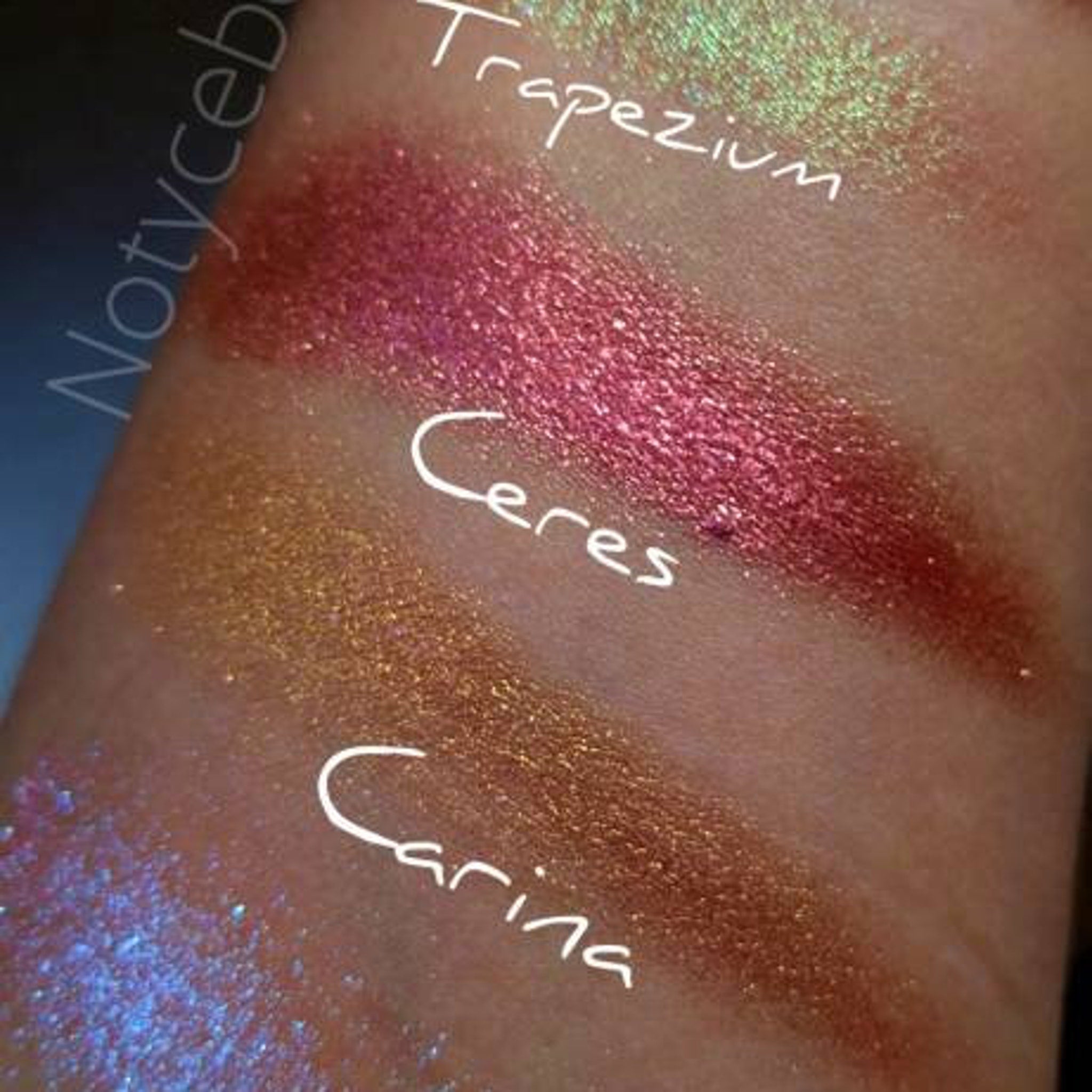 Swatch of NEBULA eyeshadow showcasing vibrant chameleon shift from orange to pink, gold, and violet on skin