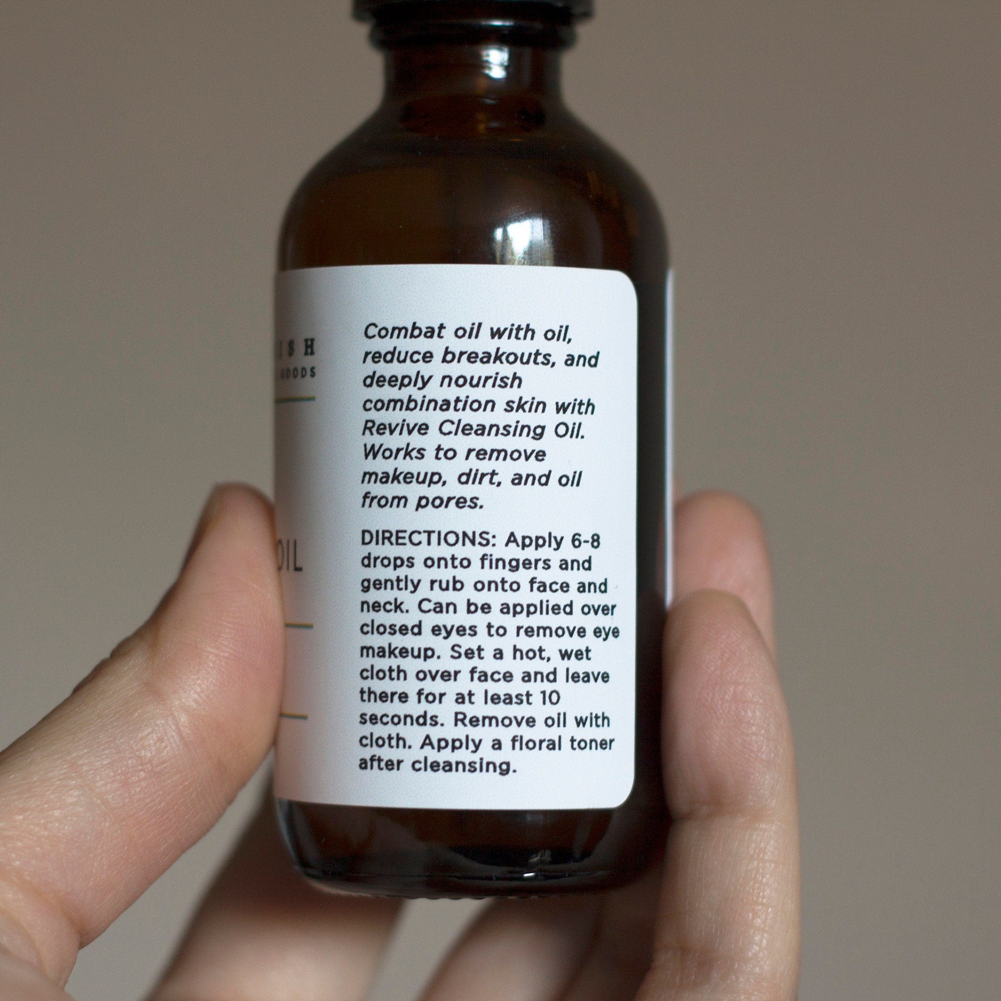 Facial cleansing oil in brown glass bottle with white label, held in hand