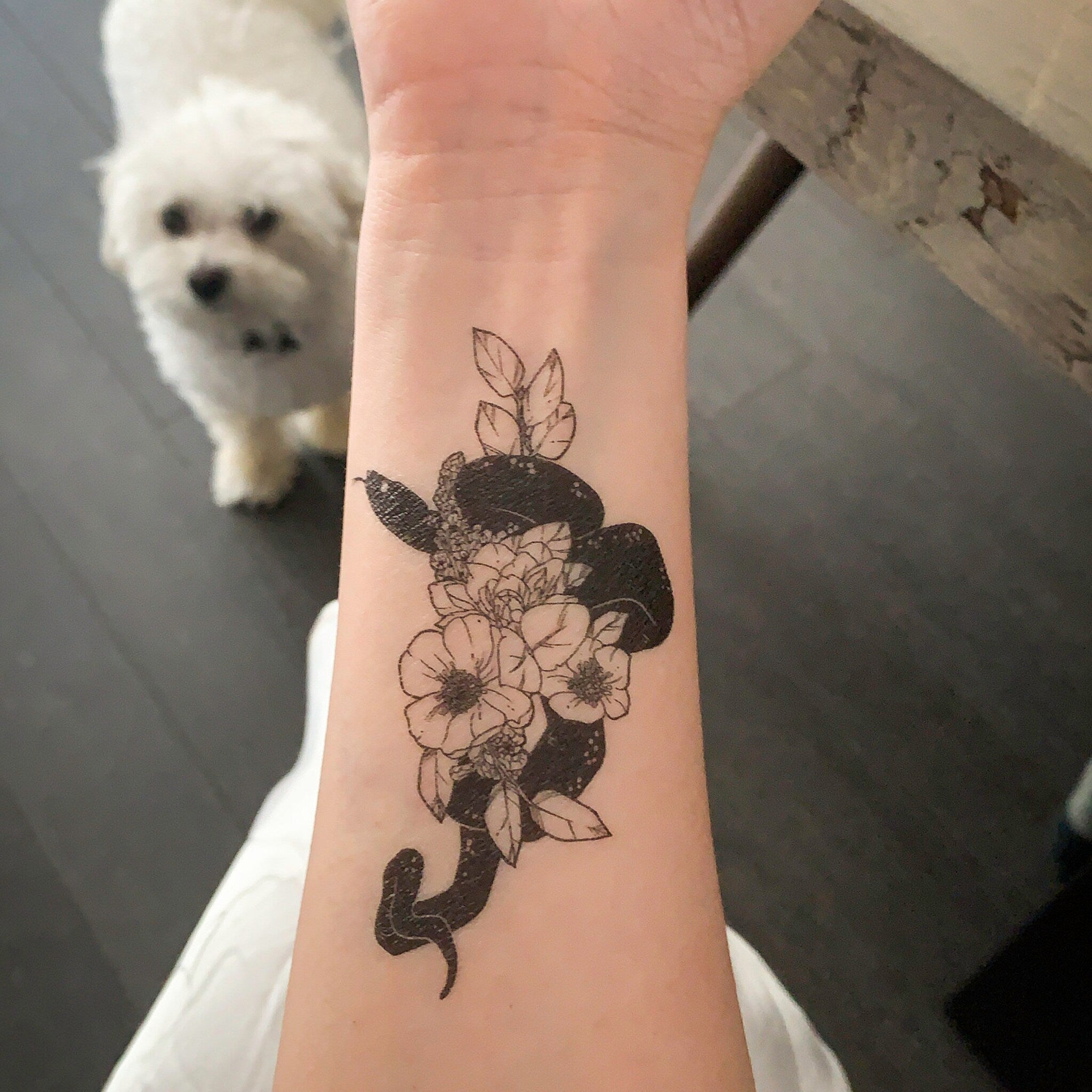 Temporary tattoo with black snake and floral design on wrist, with dog in background