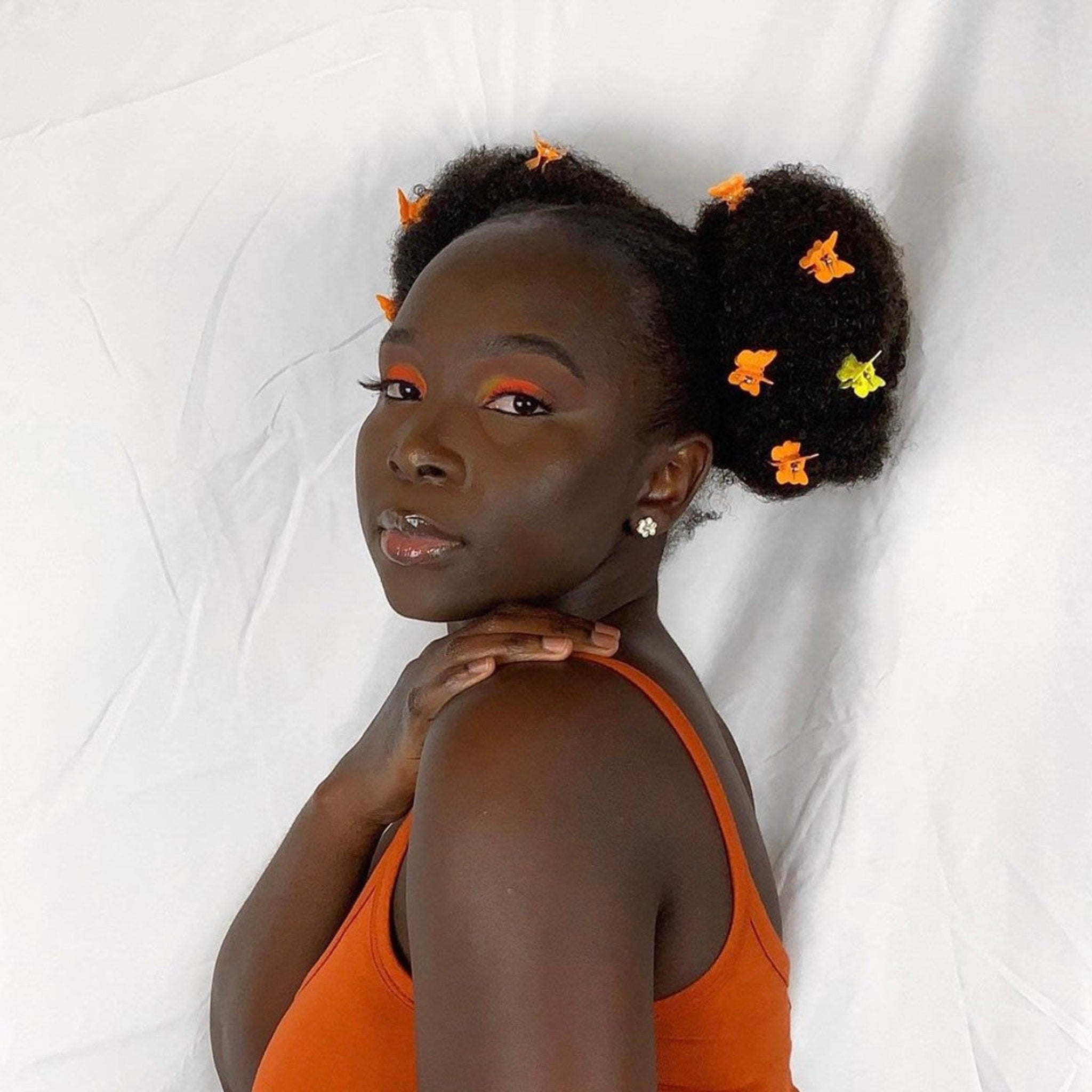 Woman with orange eye makeup and hair clips, wearing orange tank top on white background