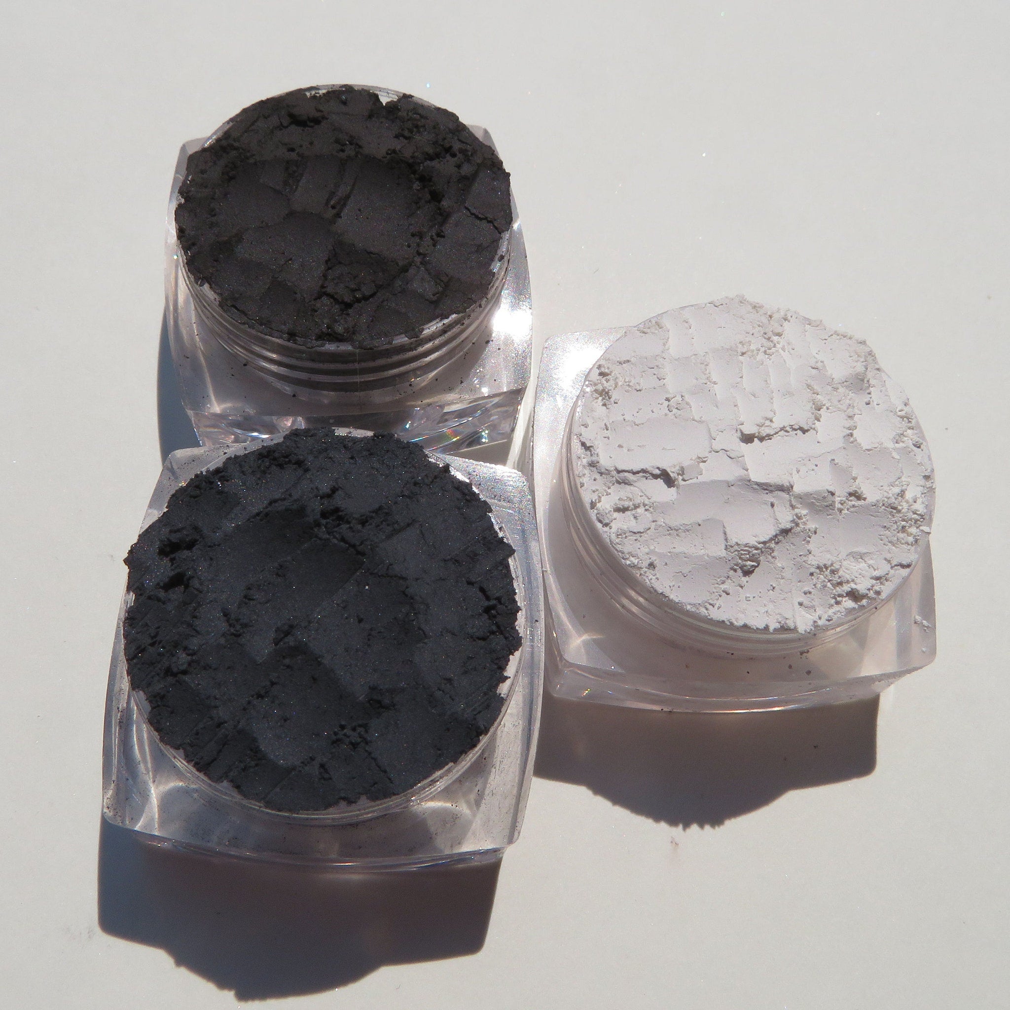 Flat lay of matte dark vegan eyeshadow palette with black eyeliner and loose powders on marble surface