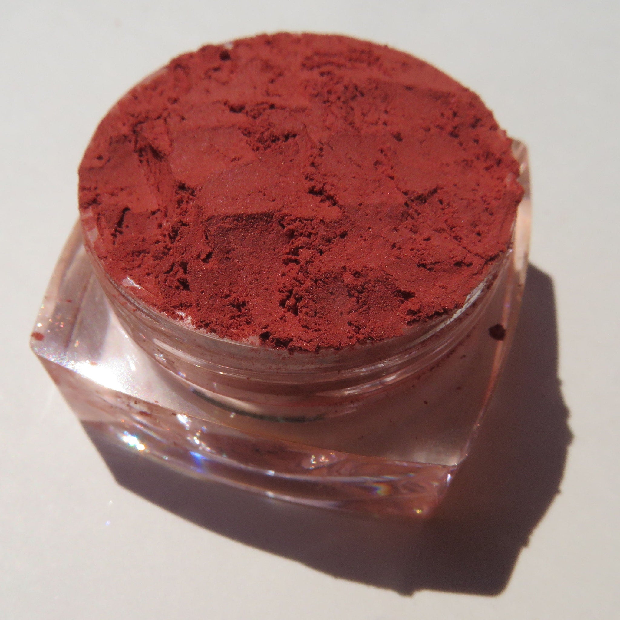 Close-up of vibrant orange-red vegan loose mineral eyeshadow with matte finish in a sifter jar