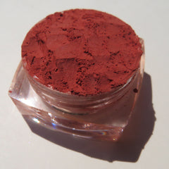 Close-up of vibrant orange-red vegan loose mineral eyeshadow with matte finish in a sifter jar