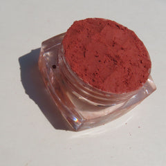 Side view of vegan matte loose mineral eyeshadow in vibrant orange-red shade, showcasing fine powder texture in jar.