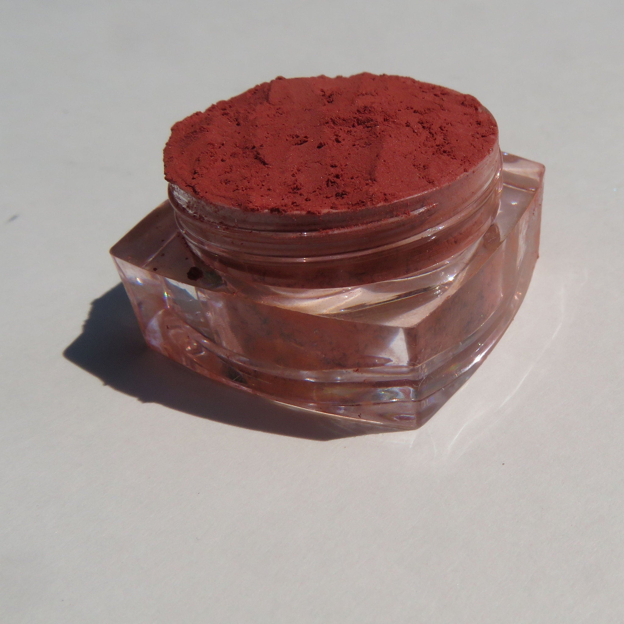 Orange red vegan loose mineral eyeshadow in a small black jar with a silver lid and matte finish.