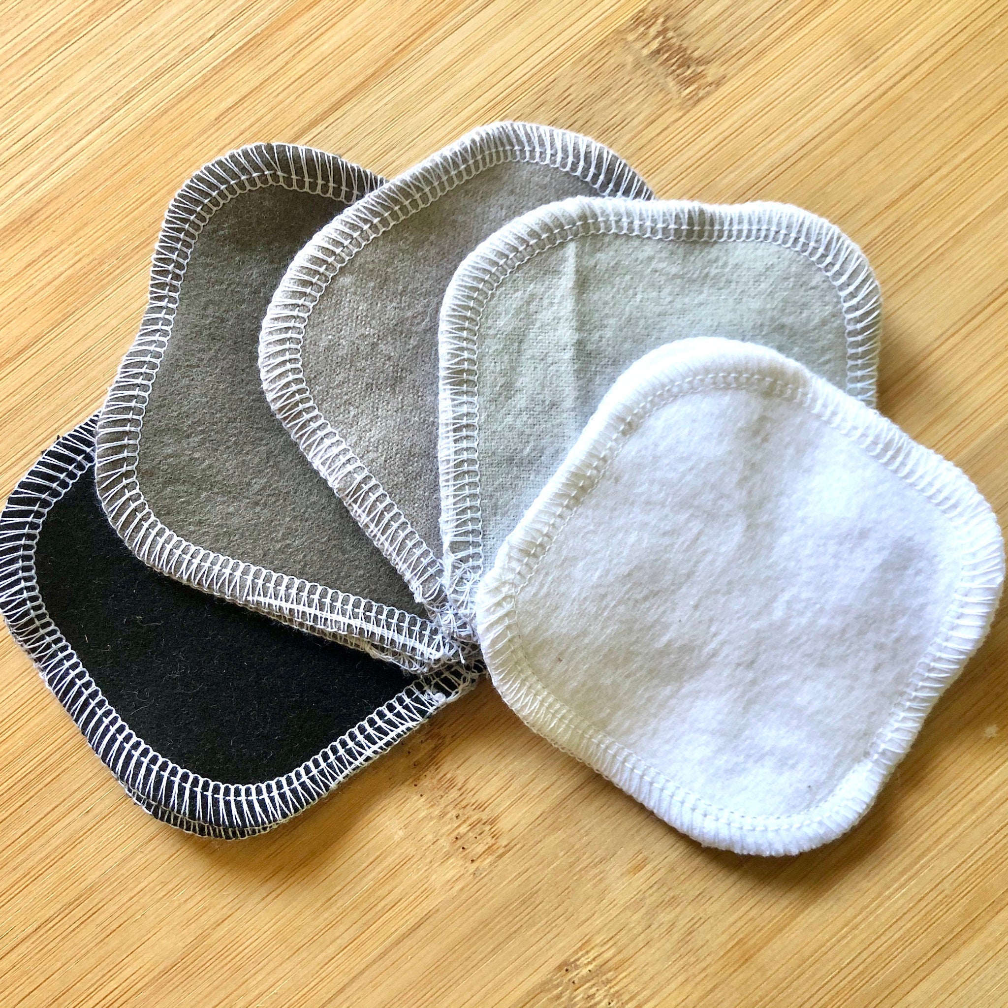 Reusable facial rounds in various colors with white stitched edging on wooden surface