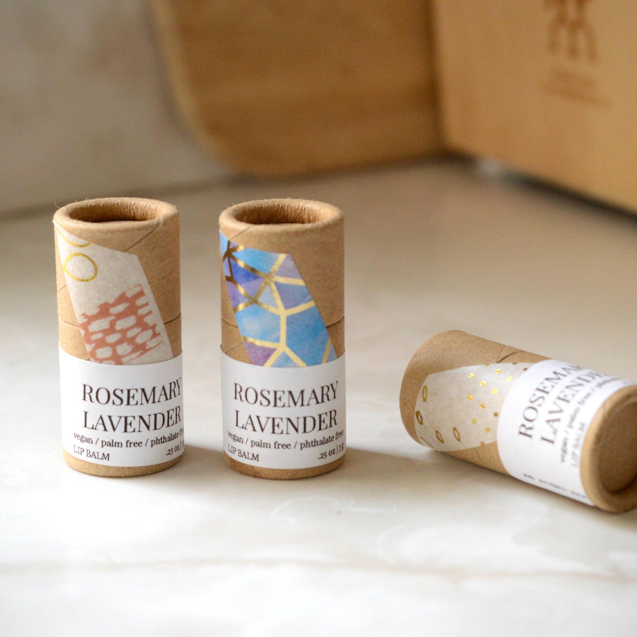 Lip balm tubes with patterned paper, brown cardboard, and white labels with text