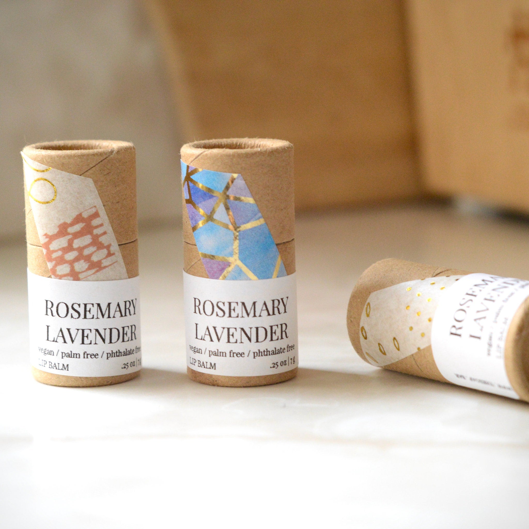 Lip balm tubes in brown cardboard with patterned paper labels, Rosemary Lavender text visible