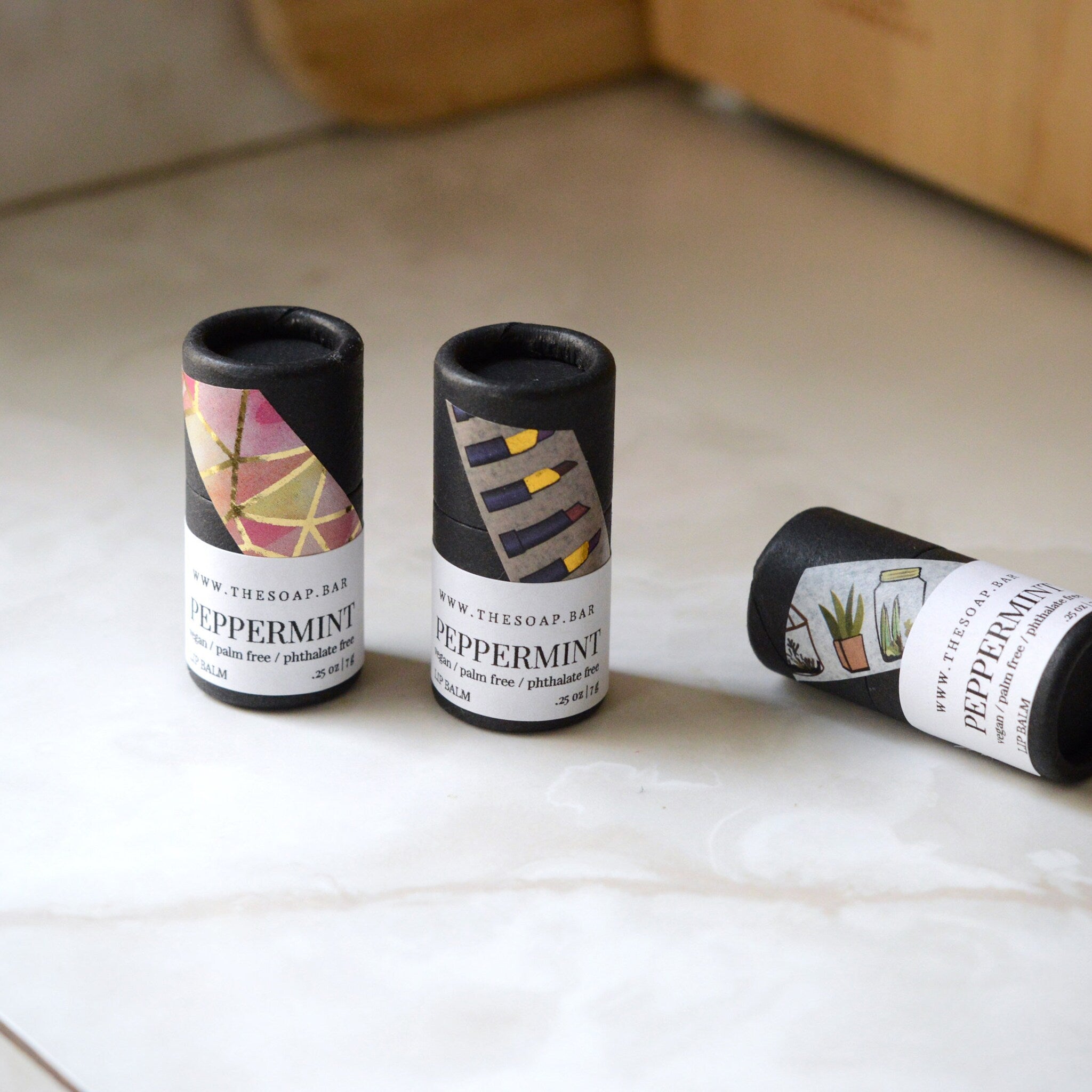 Lip balm tubes with black paper, patterned labels, and white text on a white surface