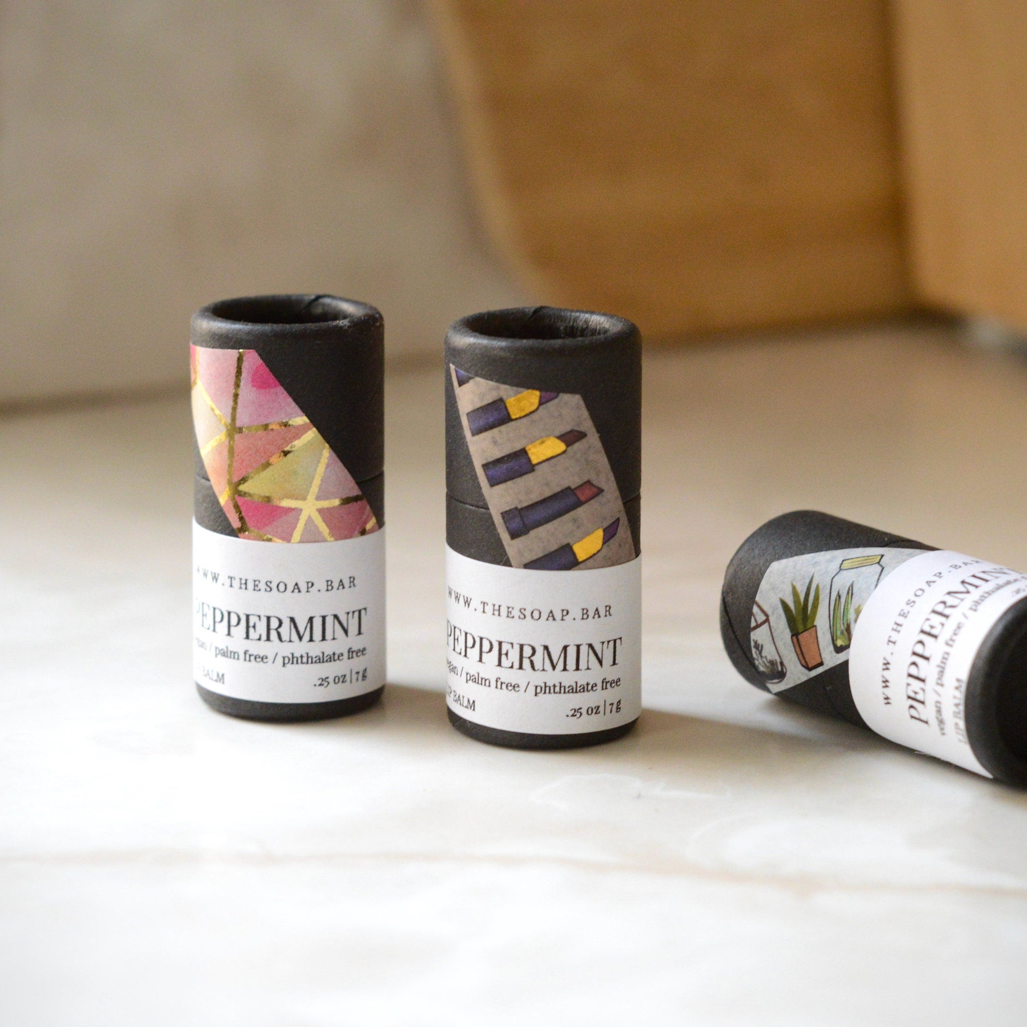 Lip balm tubes in black cardboard with patterned paper wrap and white label, "PEPERMINT" text