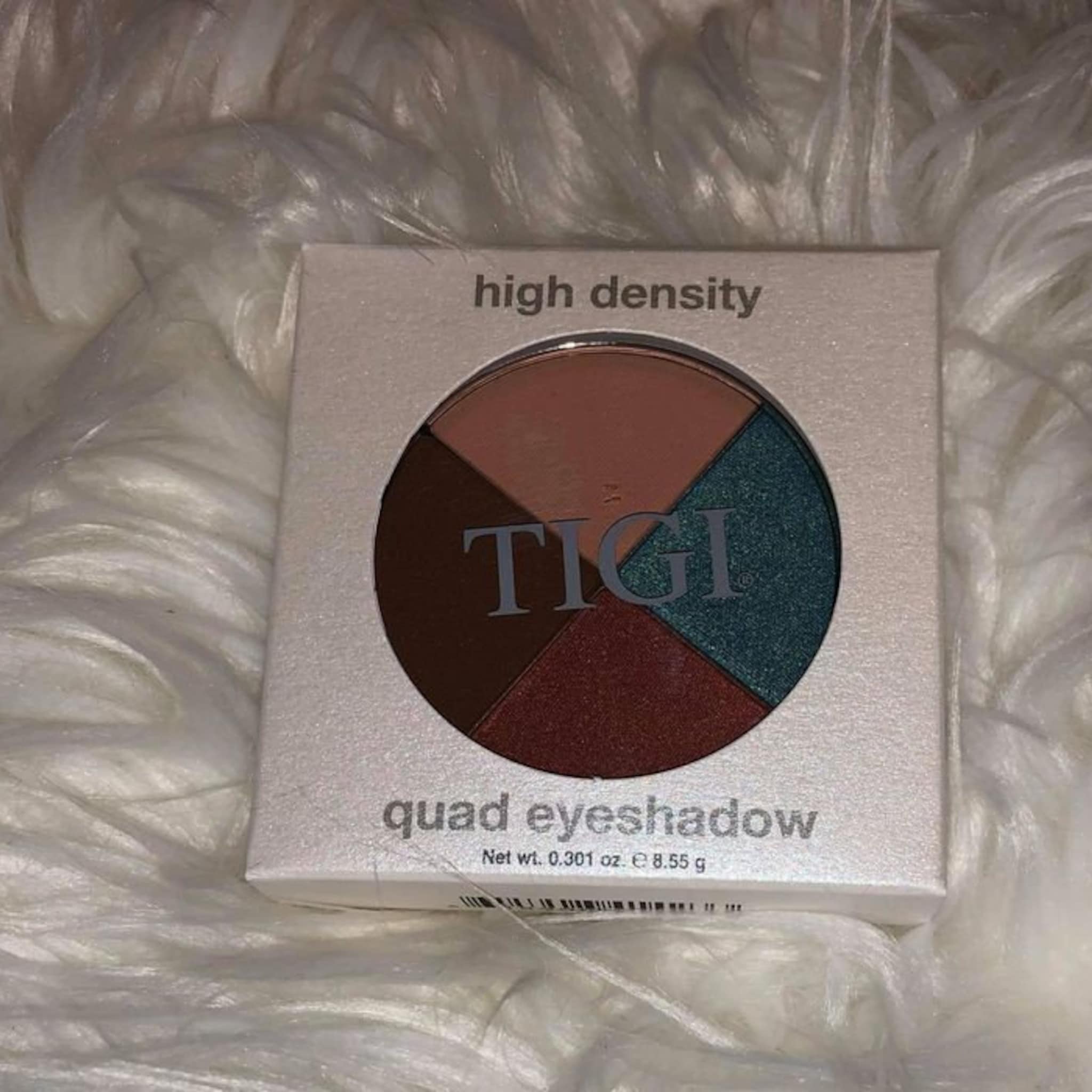 Quad eyeshadow palette with brown, red, green, and tan colors, TIGI brand name visible, in a white box
