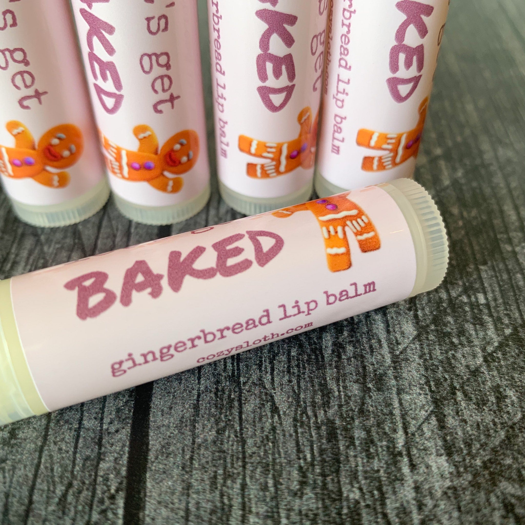 Gingerbread lip balm tubes with pink and white labels, orange gingerbread man, and "BAKED" text
