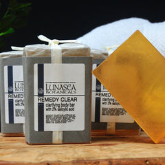 Clarifying body bars in gray boxes with LunaSea Botanicals label and gold soap piece on wood surface