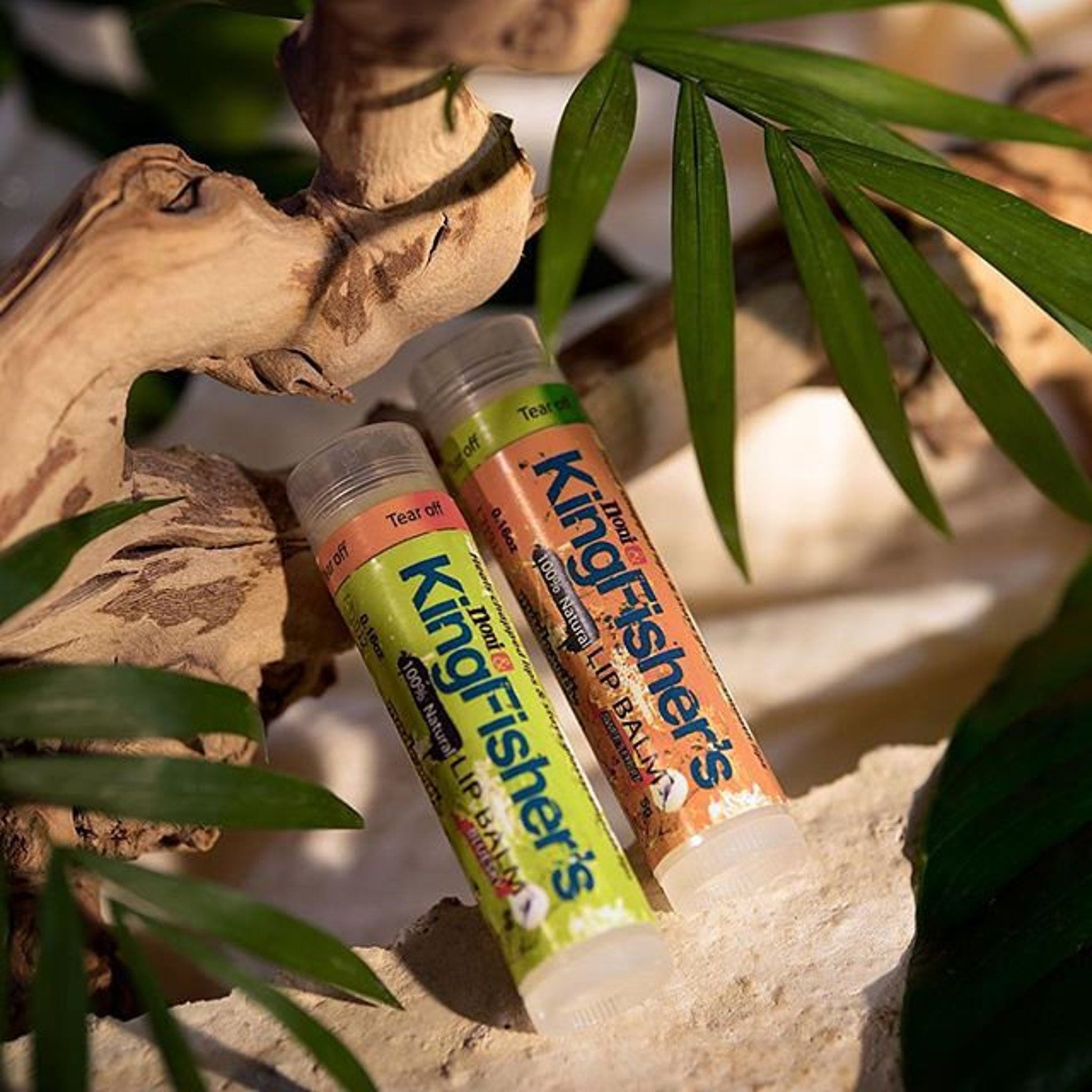 Lip balm tubes with green and orange labels, clear plastic, and KingFisher's text, on wood and leaves