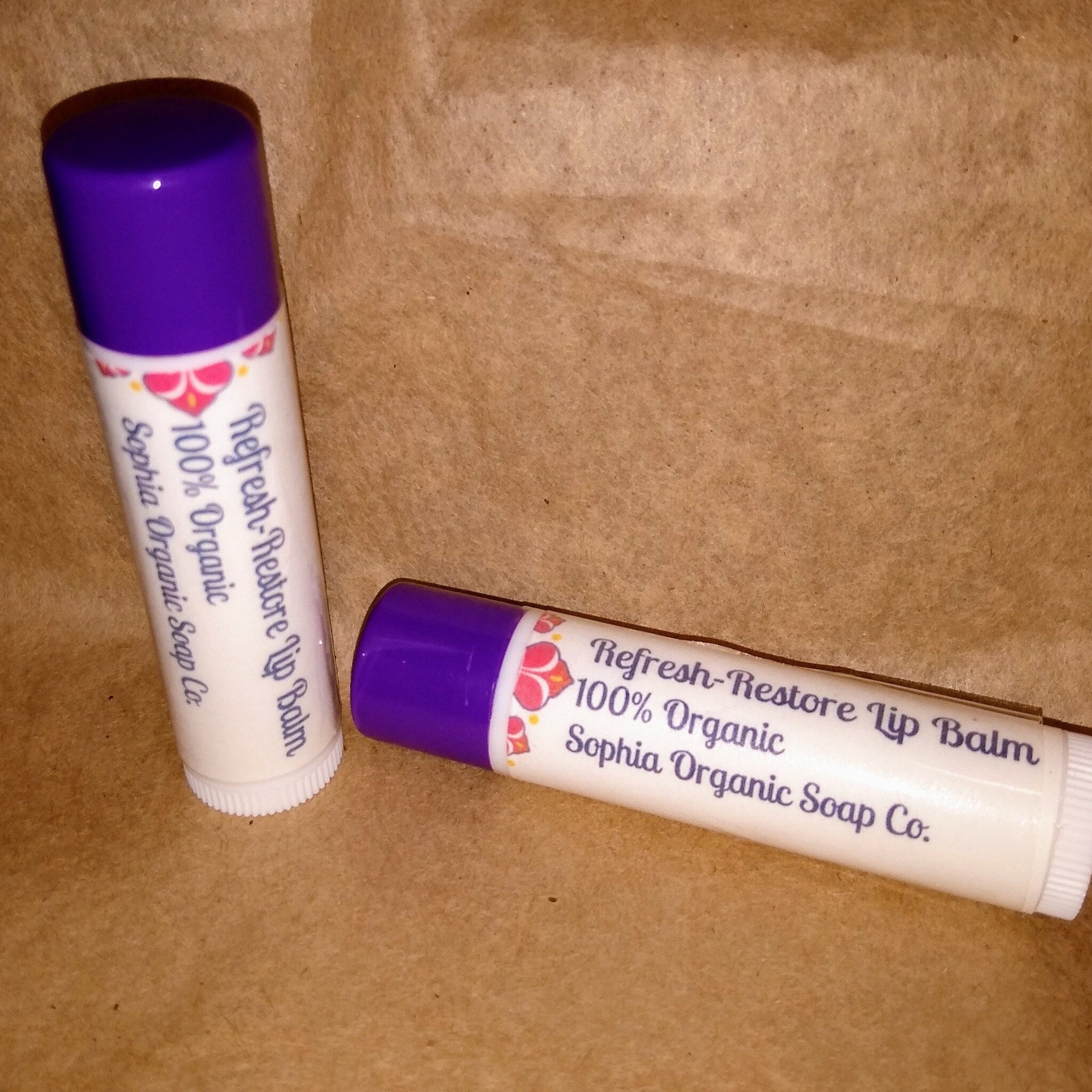 Lip balm tubes with purple caps, white tubes, and floral design, Sophia Organic Soap Co. brand visible