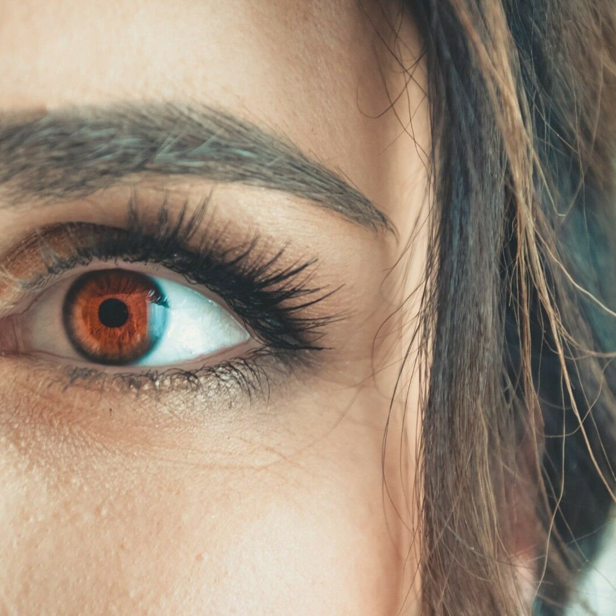 Eye close-up with brown iris, long black eyelashes, and brown hair partially visible