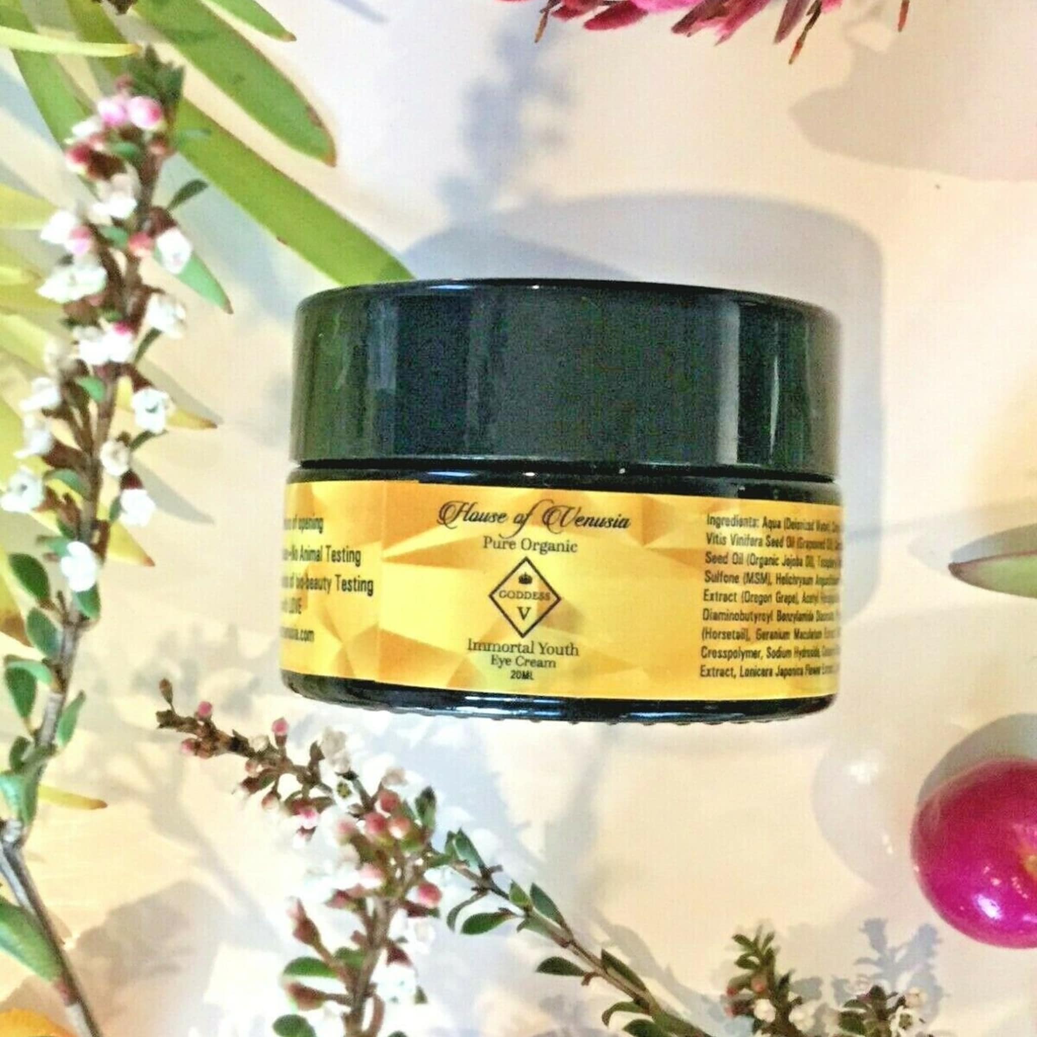 Eye cream jar with black lid and yellow label, "House of Venusia" branding visible, surrounded by flowers