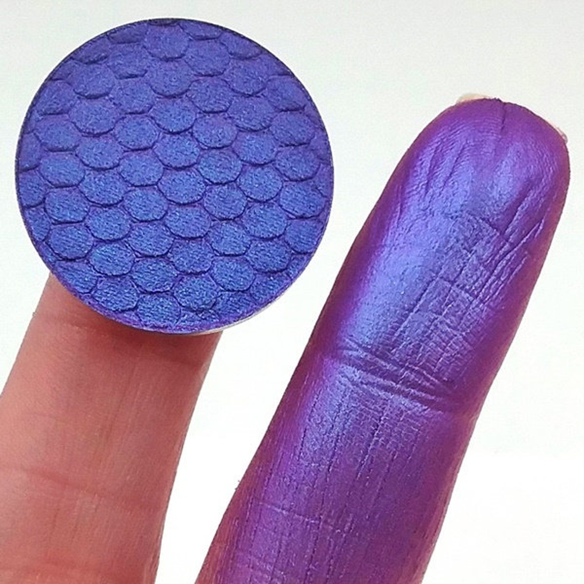 Side view of duochrome blurple eyeshadow pan showing color shift from blue to purple in angled lighting