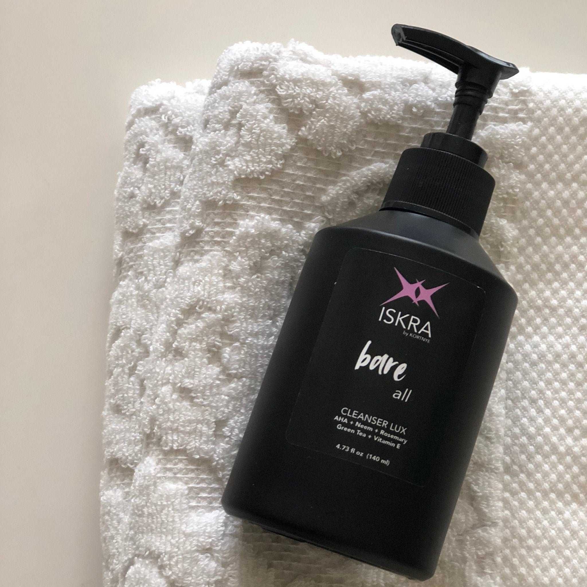 Cleanser bottle on white patterned towel, black bottle with ISKRA branding and pump top
