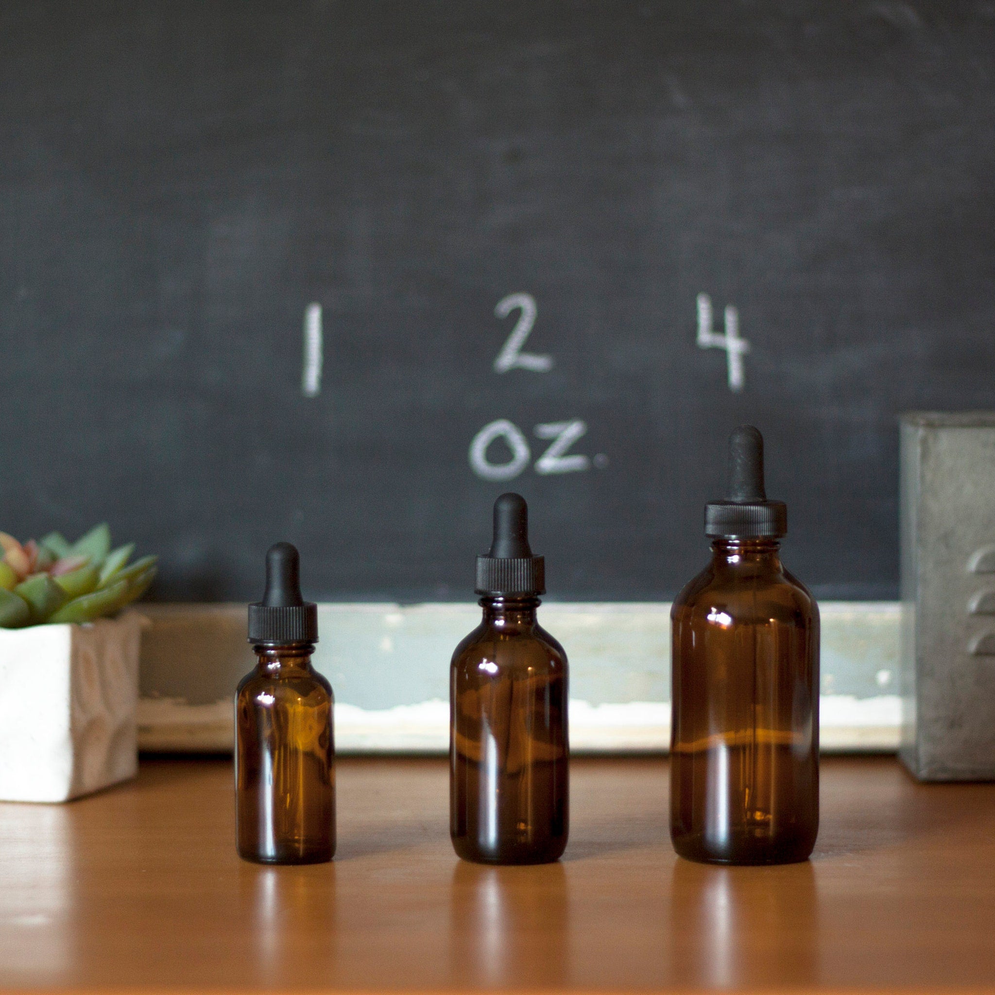 Amber glass dropper bottles with black droppers, displayed on a wood surface, with chalkboard background