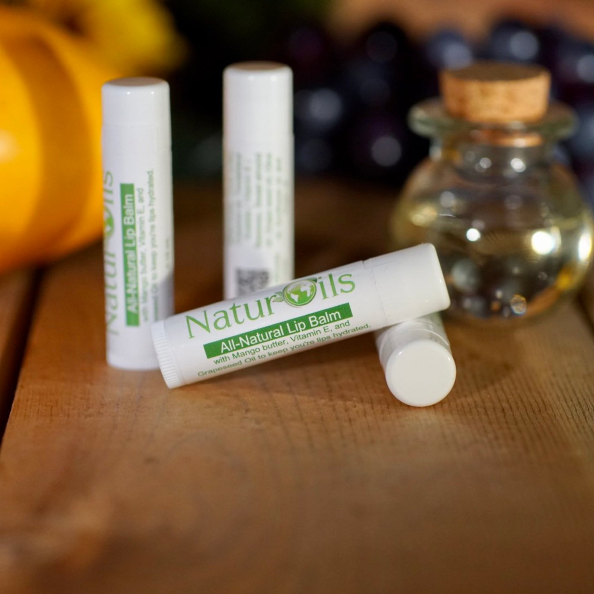 Lip balm tubes, white with green text, NaturOils brand, on wooden surface