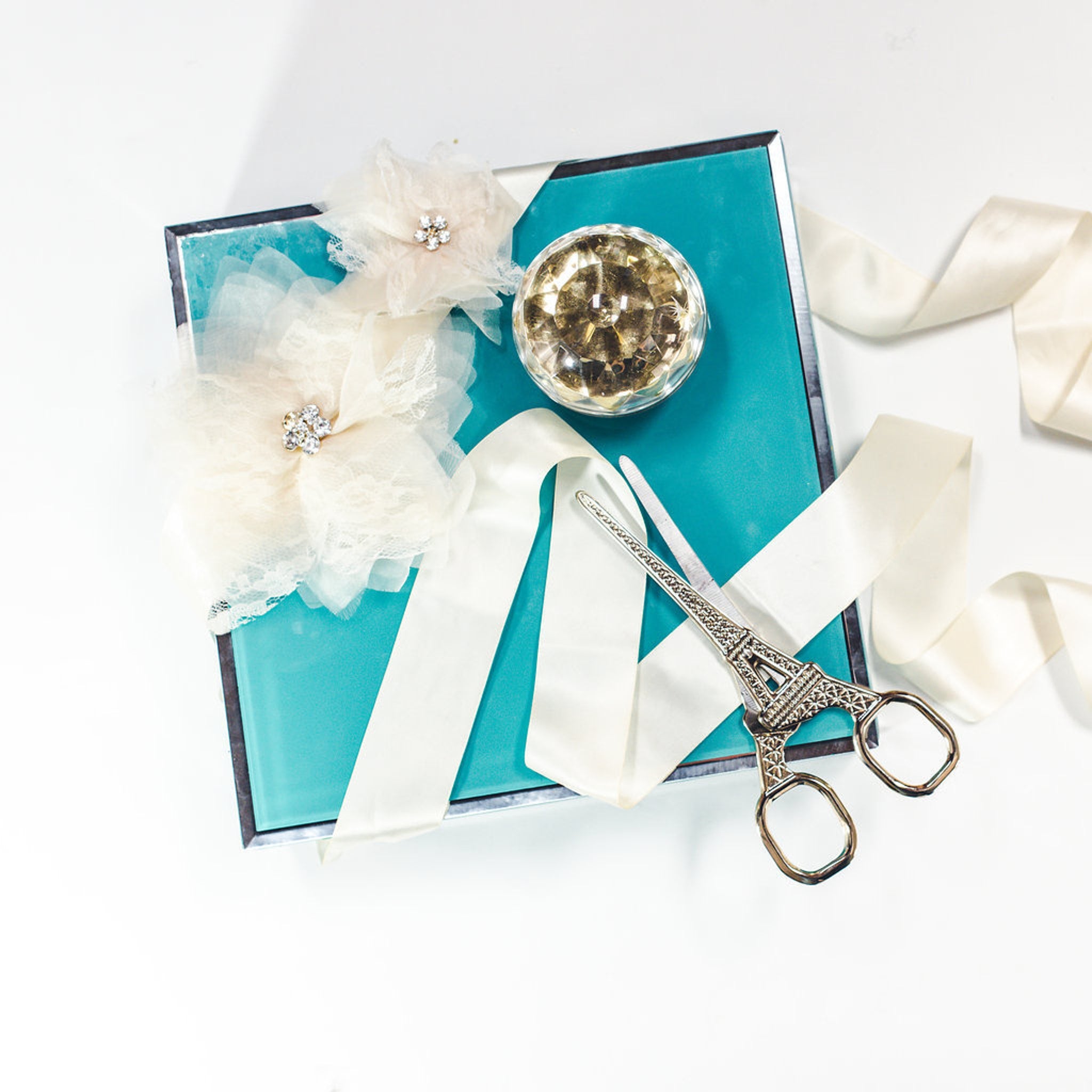 Scissors with Eiffel Tower design, turquoise box, cream ribbon, and floral accents on white background