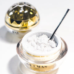 Facial cleanser with white crystals, glass jar, gold rim, and silver spoon in use