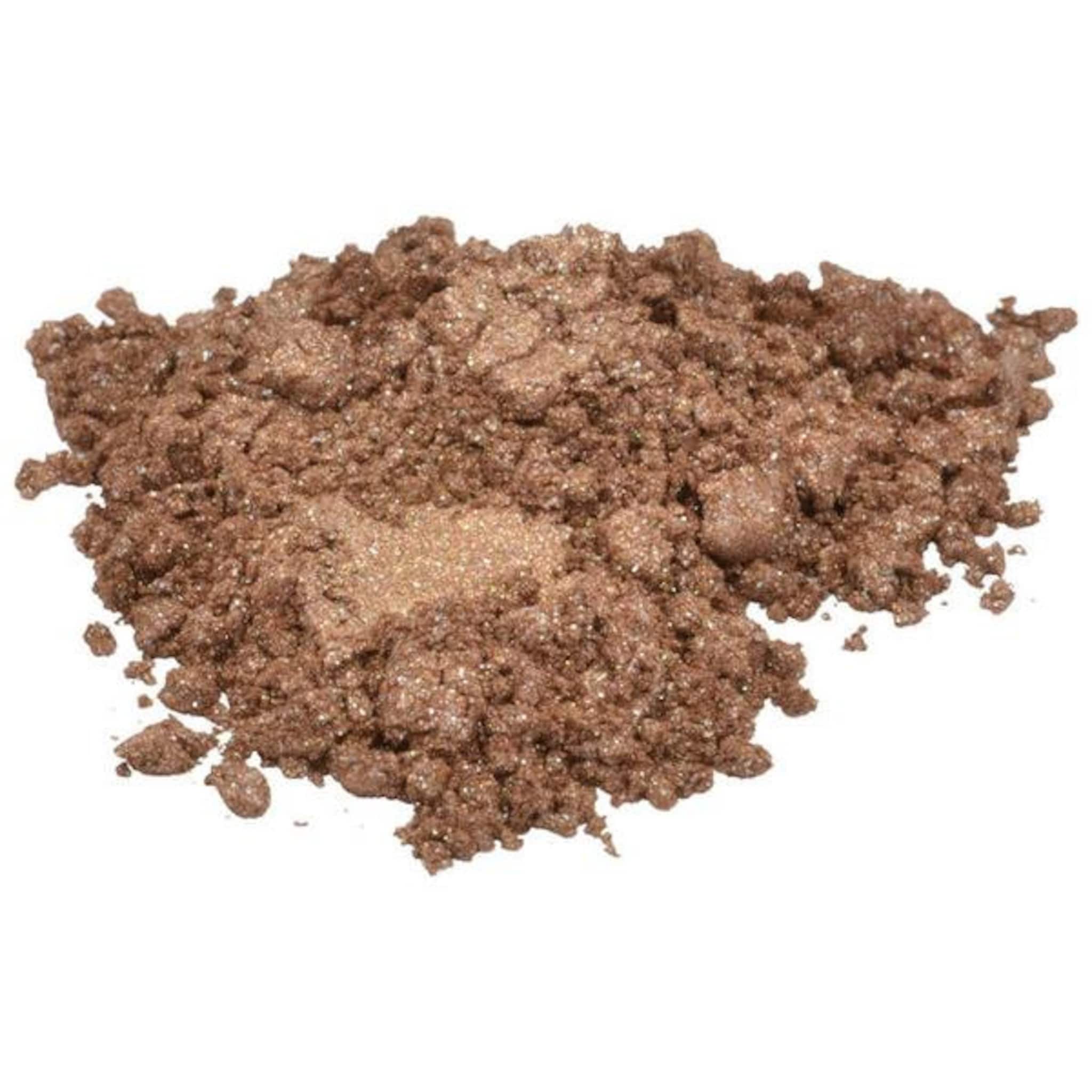 Close-up of shimmering brown sienna mica powder spilling from an open container, showcasing fine pigment texture
