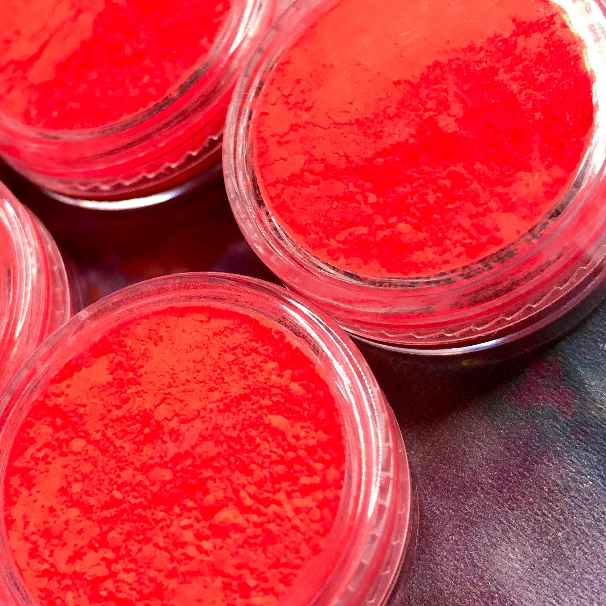 Vibrant red eyeshadow pigment pot with gold lid displayed on a sleek black surface.