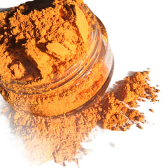 Orange powder spilling from a clear glass jar on a white surface
