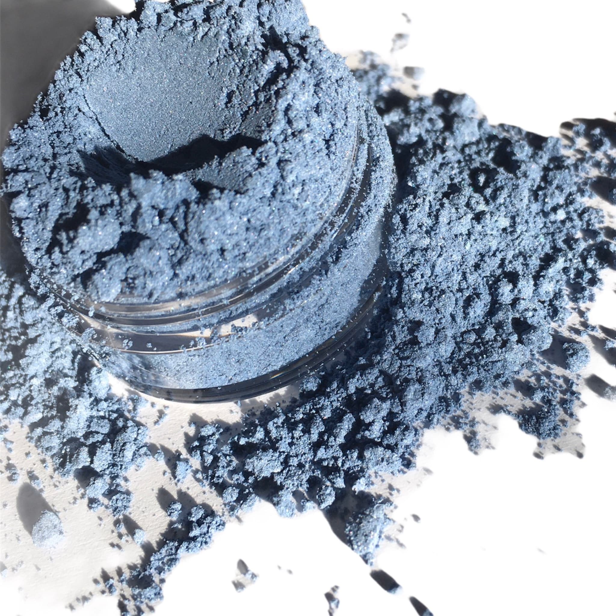 Blue powder eyeshadow, loose powder, with glass jar, and scattered powder on white surface